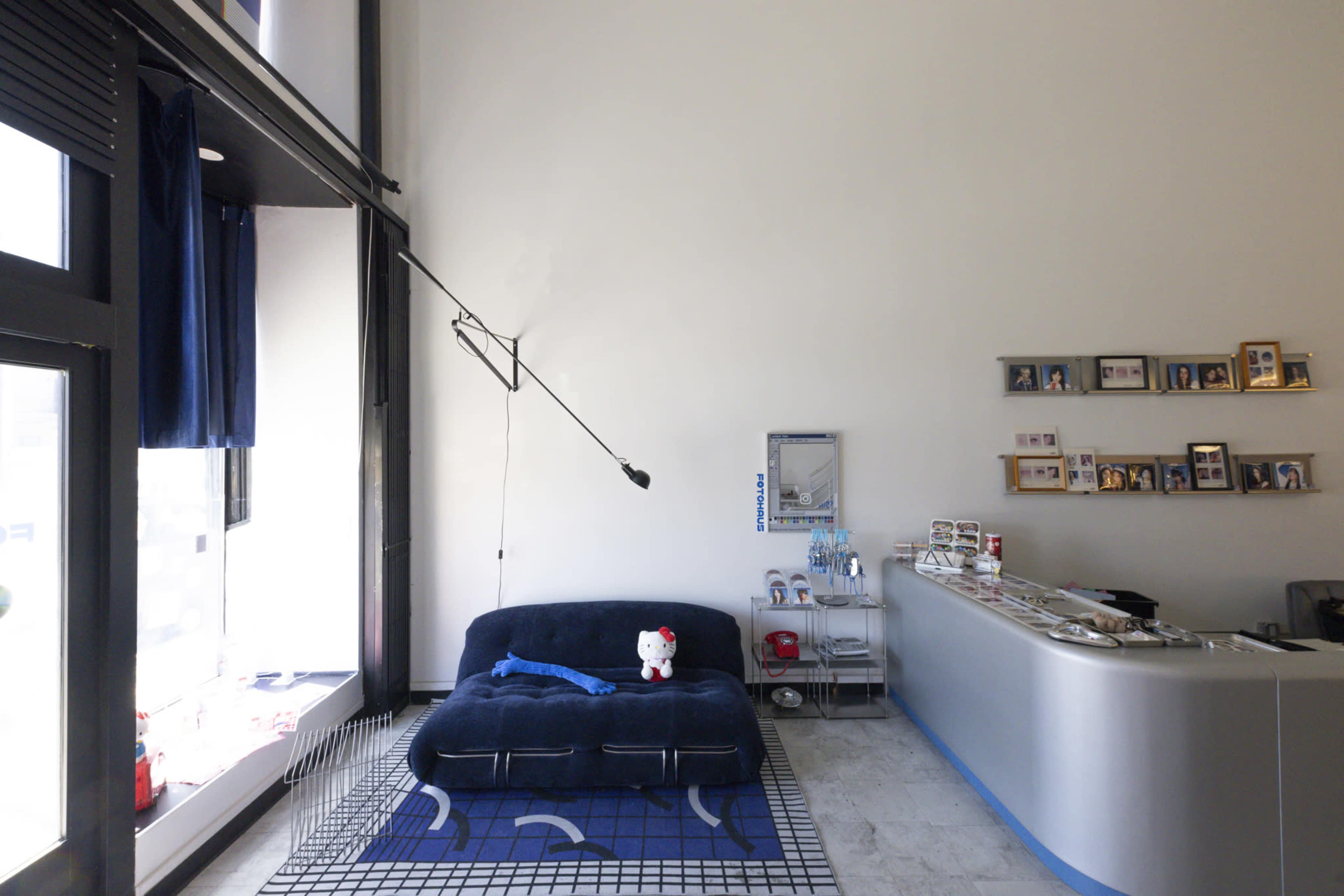 The image shows a modern reception area featuring a blue sofa, a blue patterned rug, and a white service counter with shelves displaying framed photos.