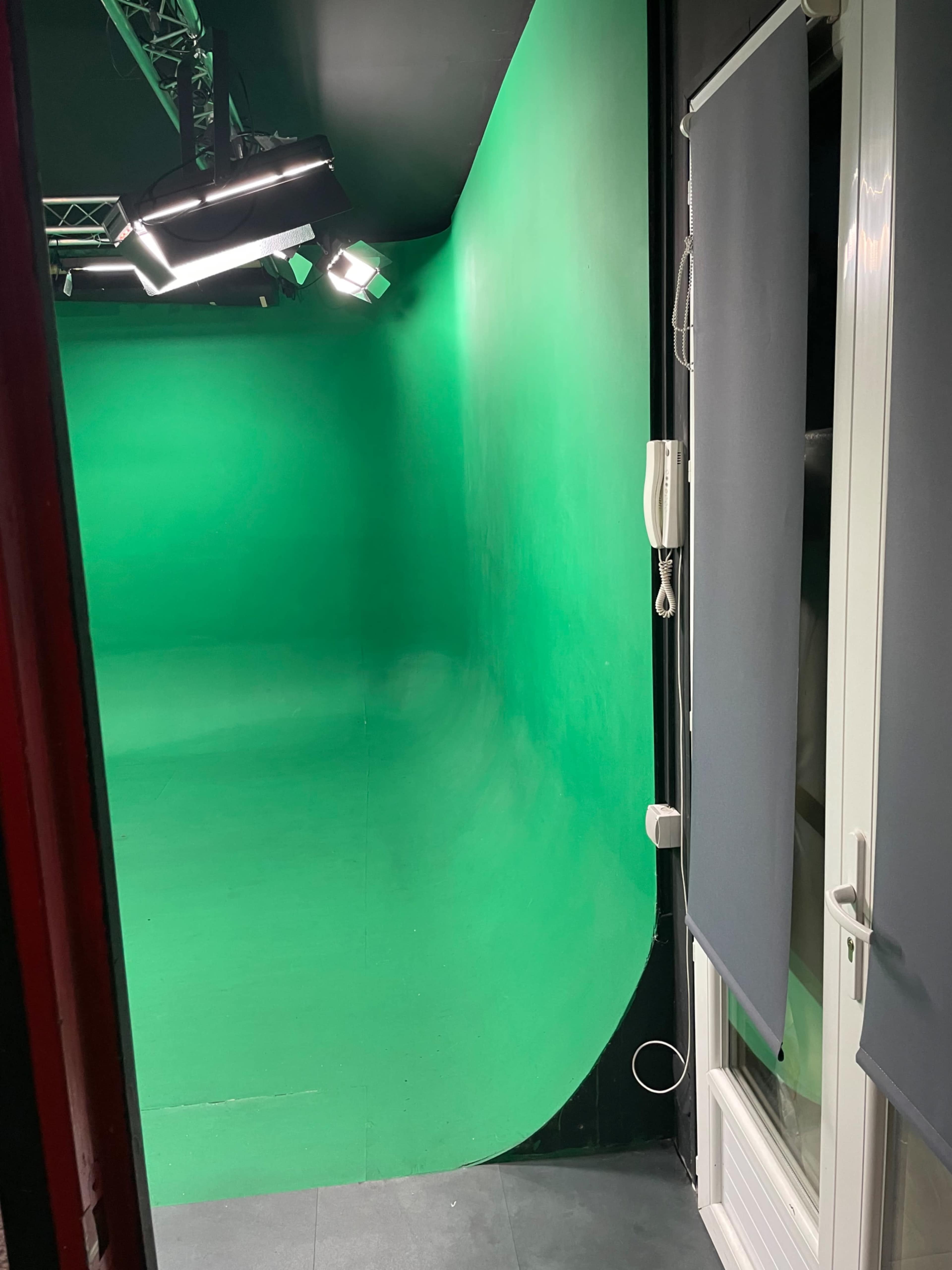 The image shows a green screen studio with a curved green backdrop and a door partially opened on the right side.