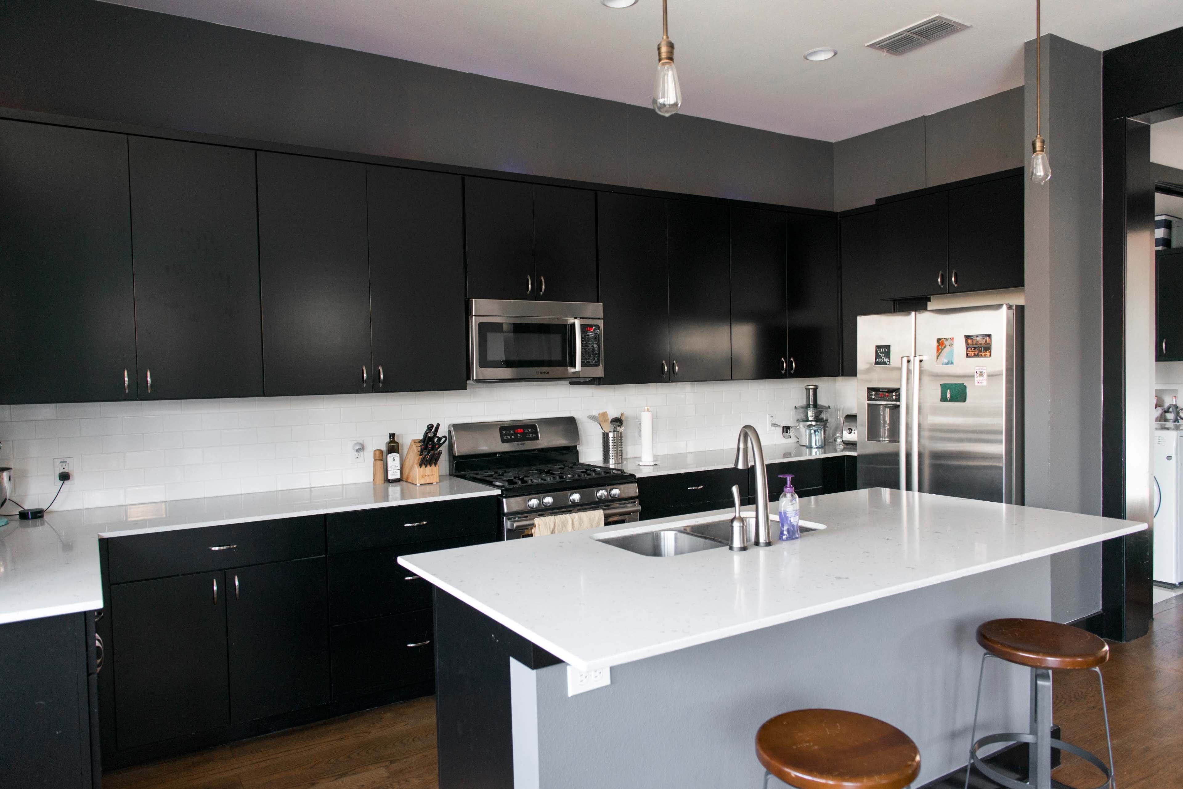 The kitchen features black cabinetry, a stainless steel refrigerator, and an island with bar stools.