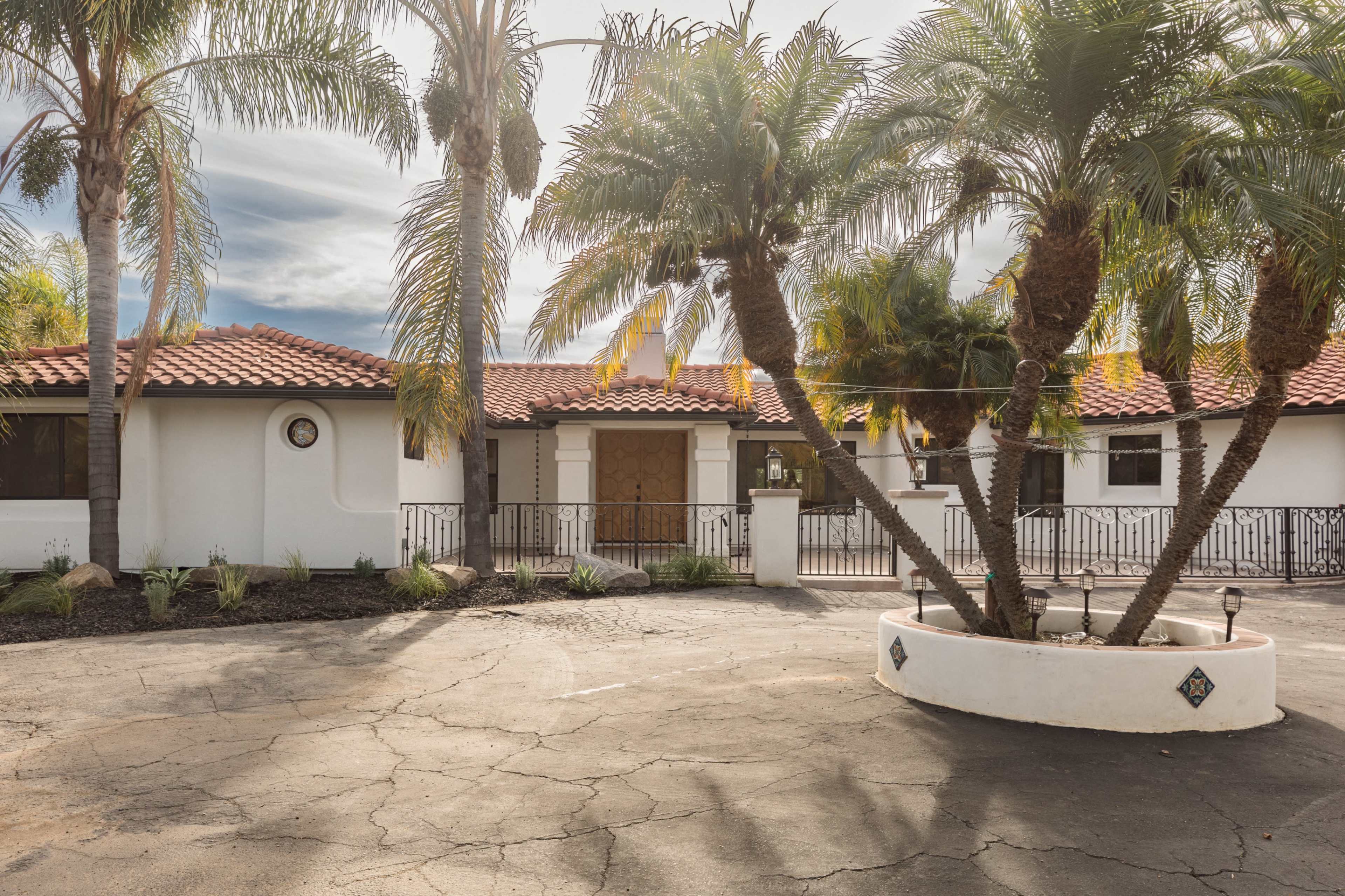 A courtyard features a circular planter with palm trees and a Spanish-style home in the background.