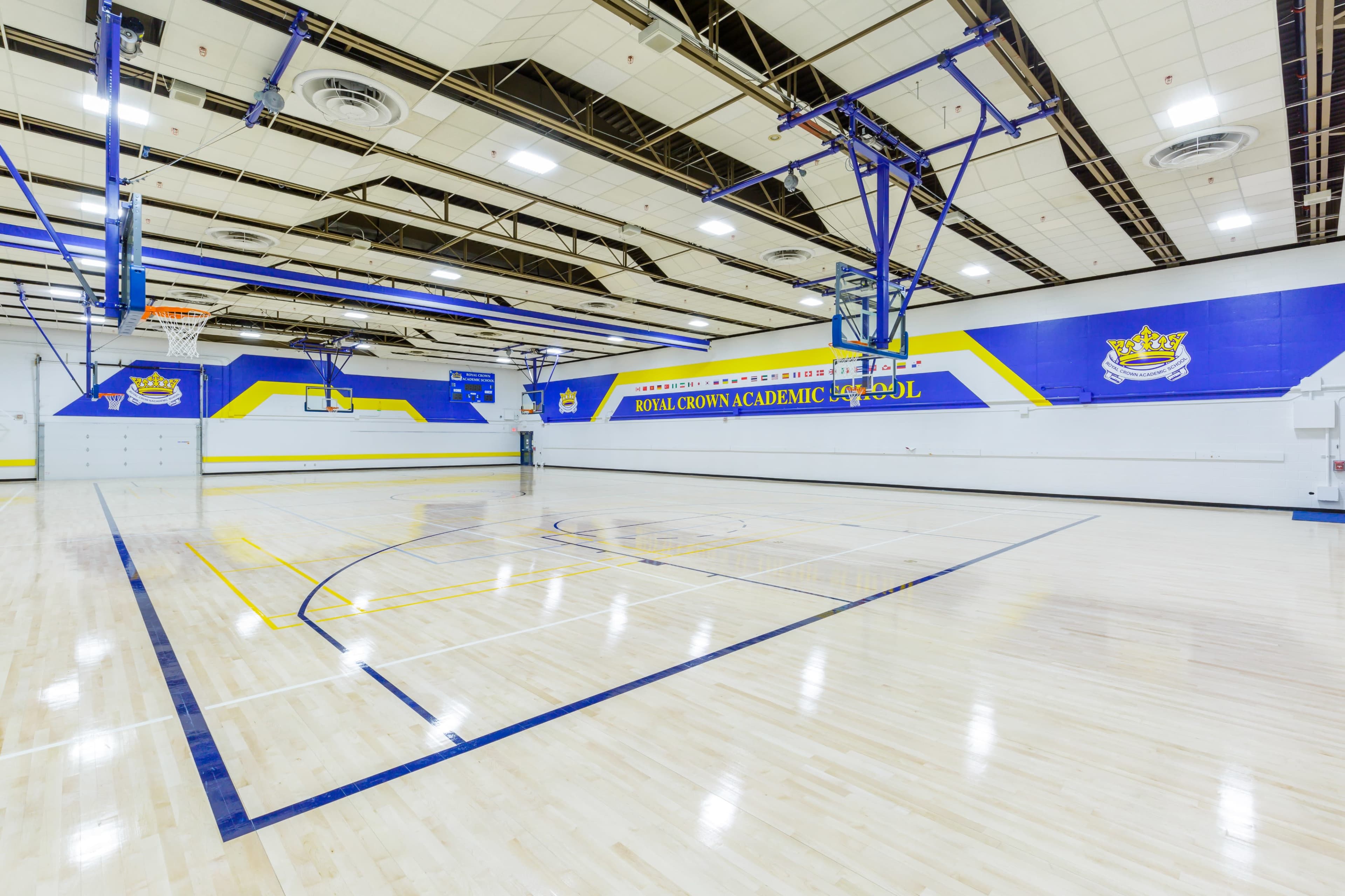The image shows a brightly lit indoor basketball court featuring two basketball hoops and painted walls with a school logo and colors.