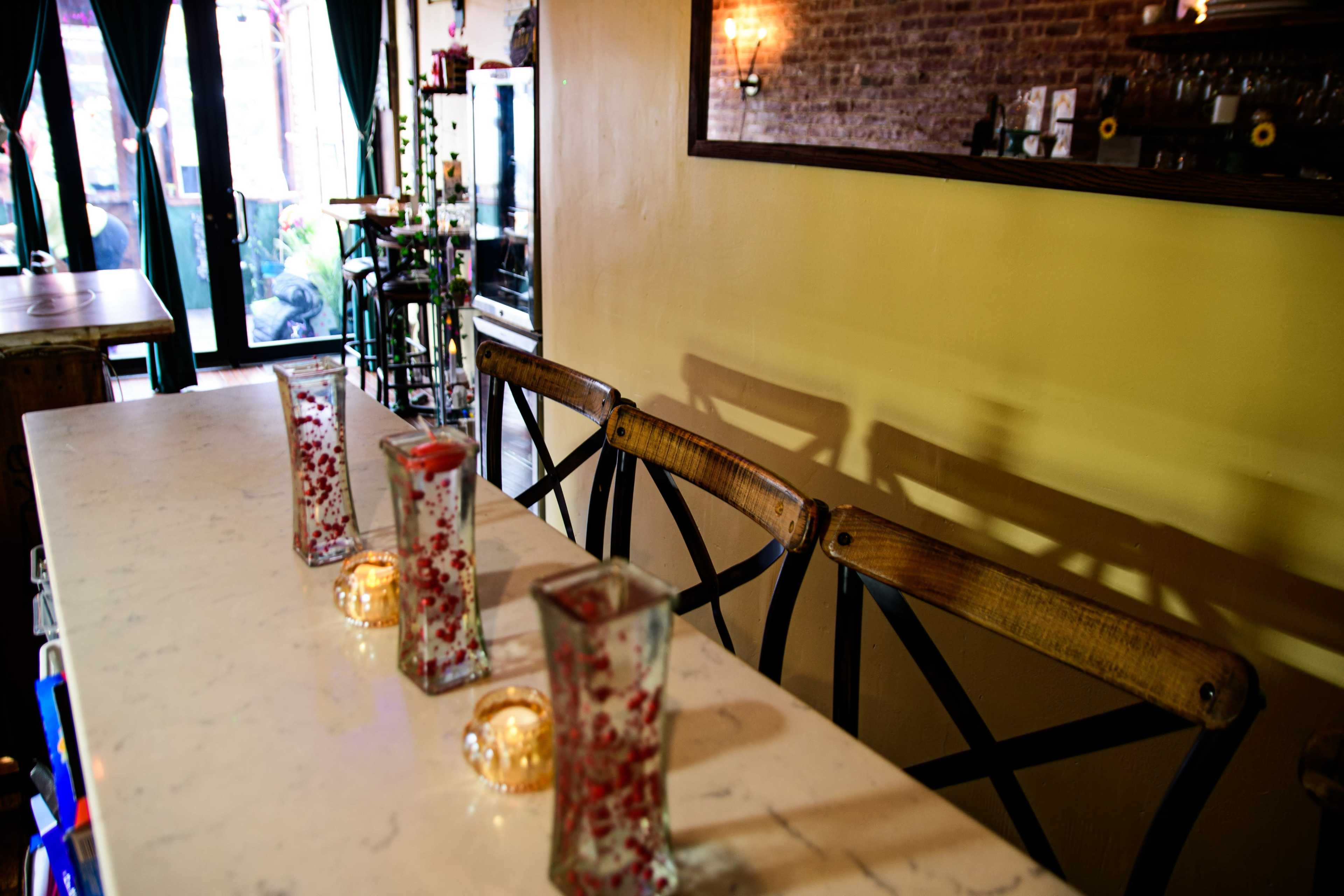 A bar countertop with four decorative vases and candles placed along its length, against a background of yellow walls and a mirror.