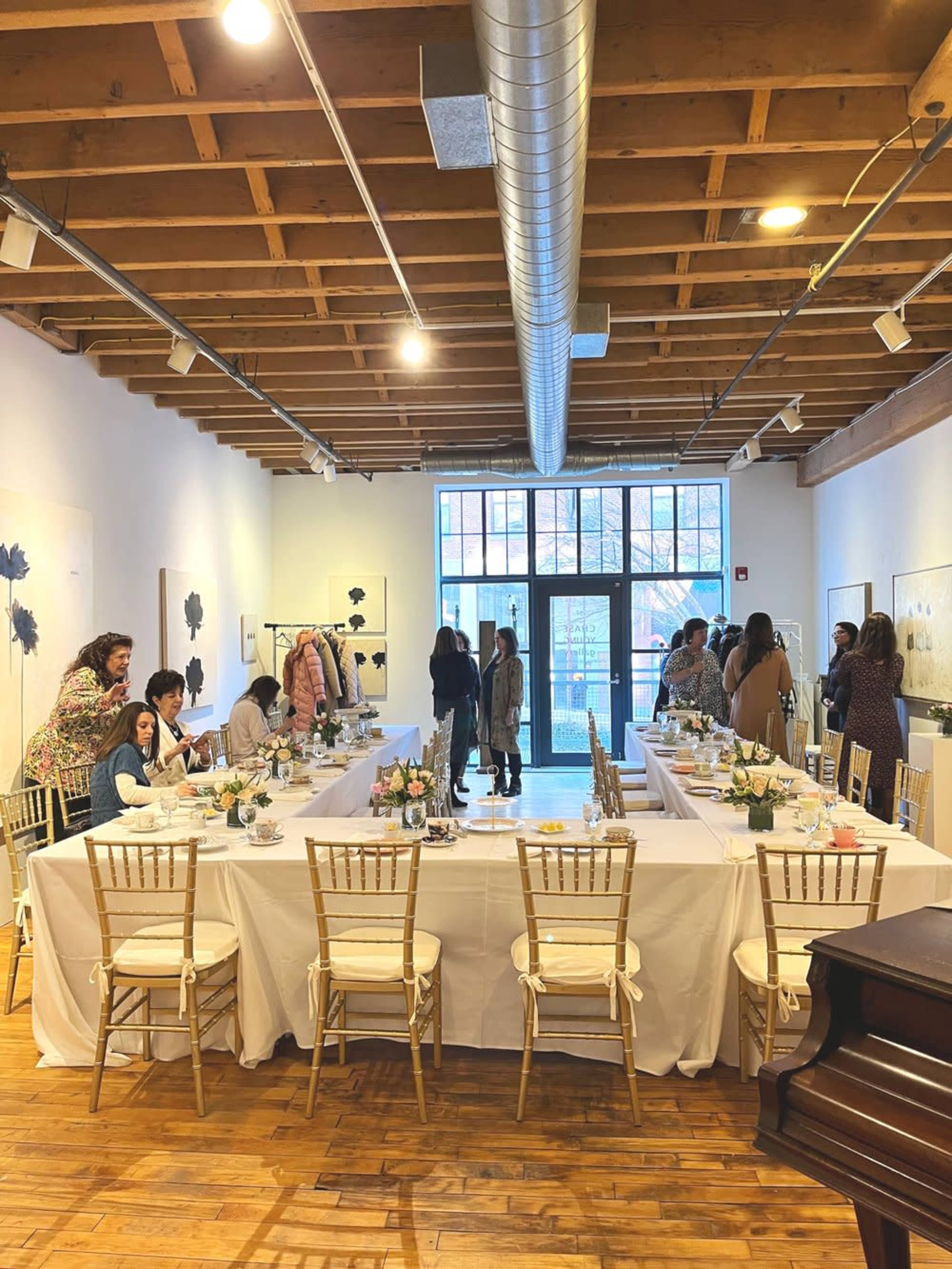 A large dining area is set up with a long table, decorated with flowers, where guests are mingling and enjoying the surroundings.