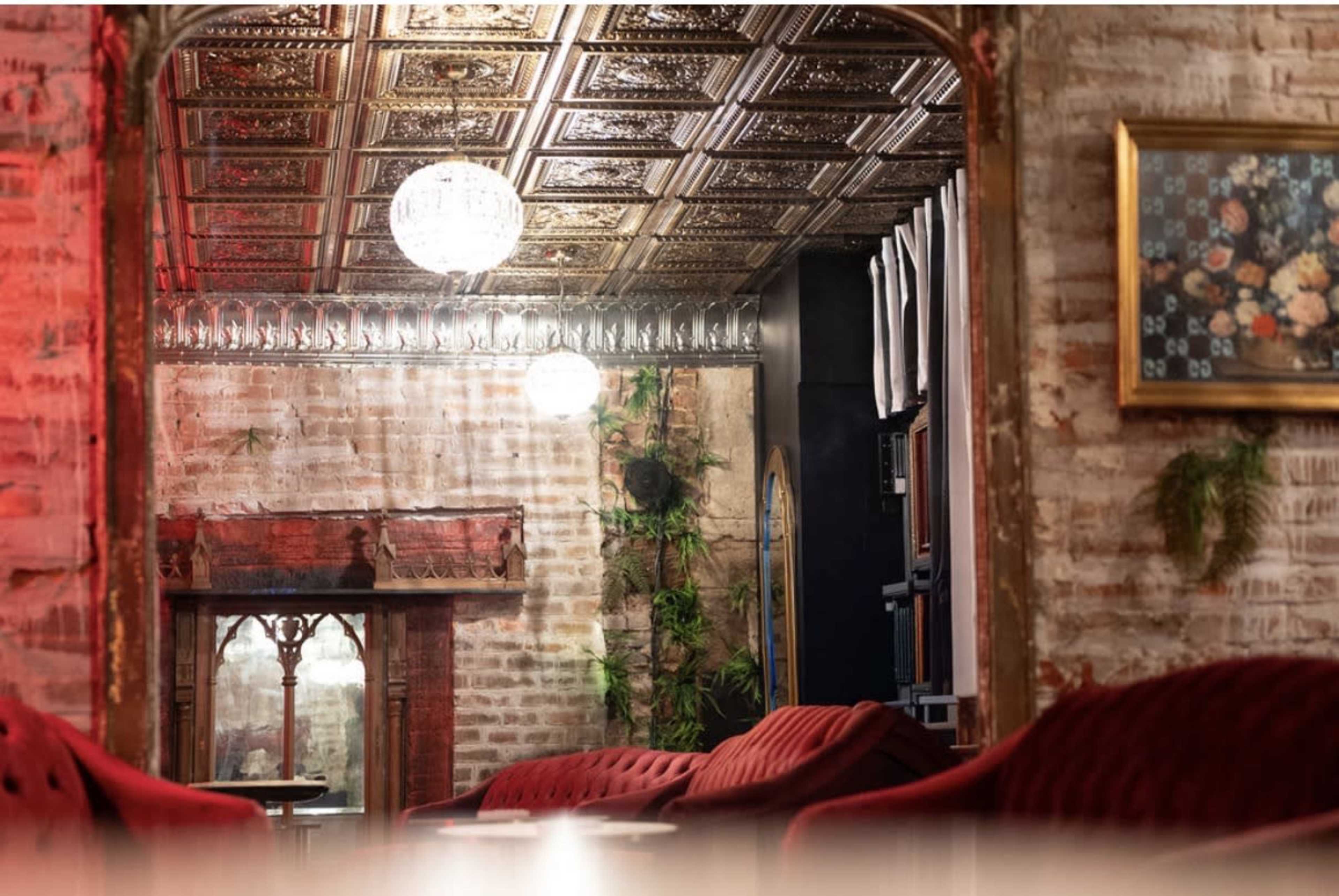 The image shows a cozy restaurant interior with vintage decor, featuring a patterned ceiling, plush red seating, and soft lighting.