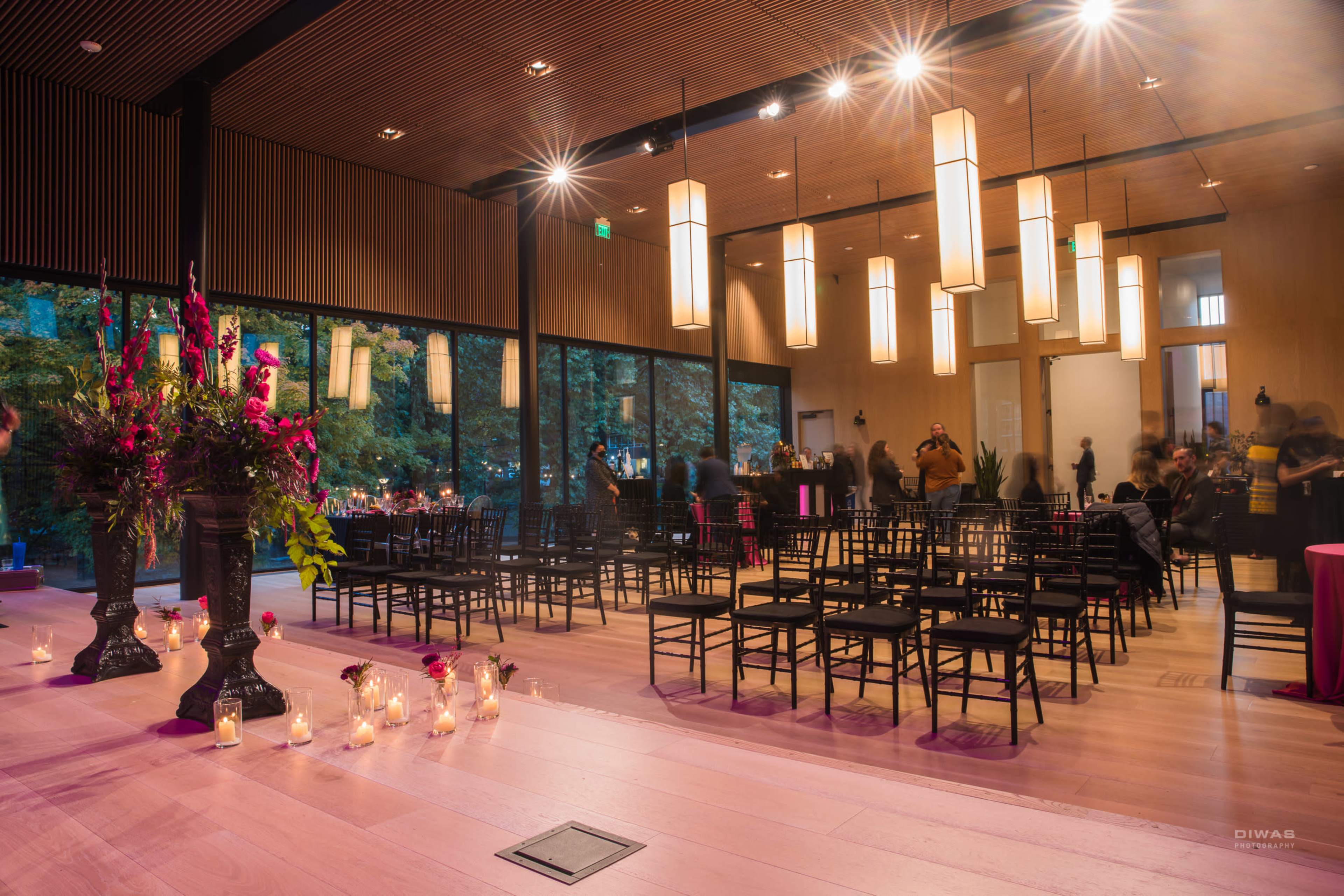 An indoor venue with rows of black chairs, a floral arrangement, and soft lighting from hanging lamps, creating a space set up for an event.
