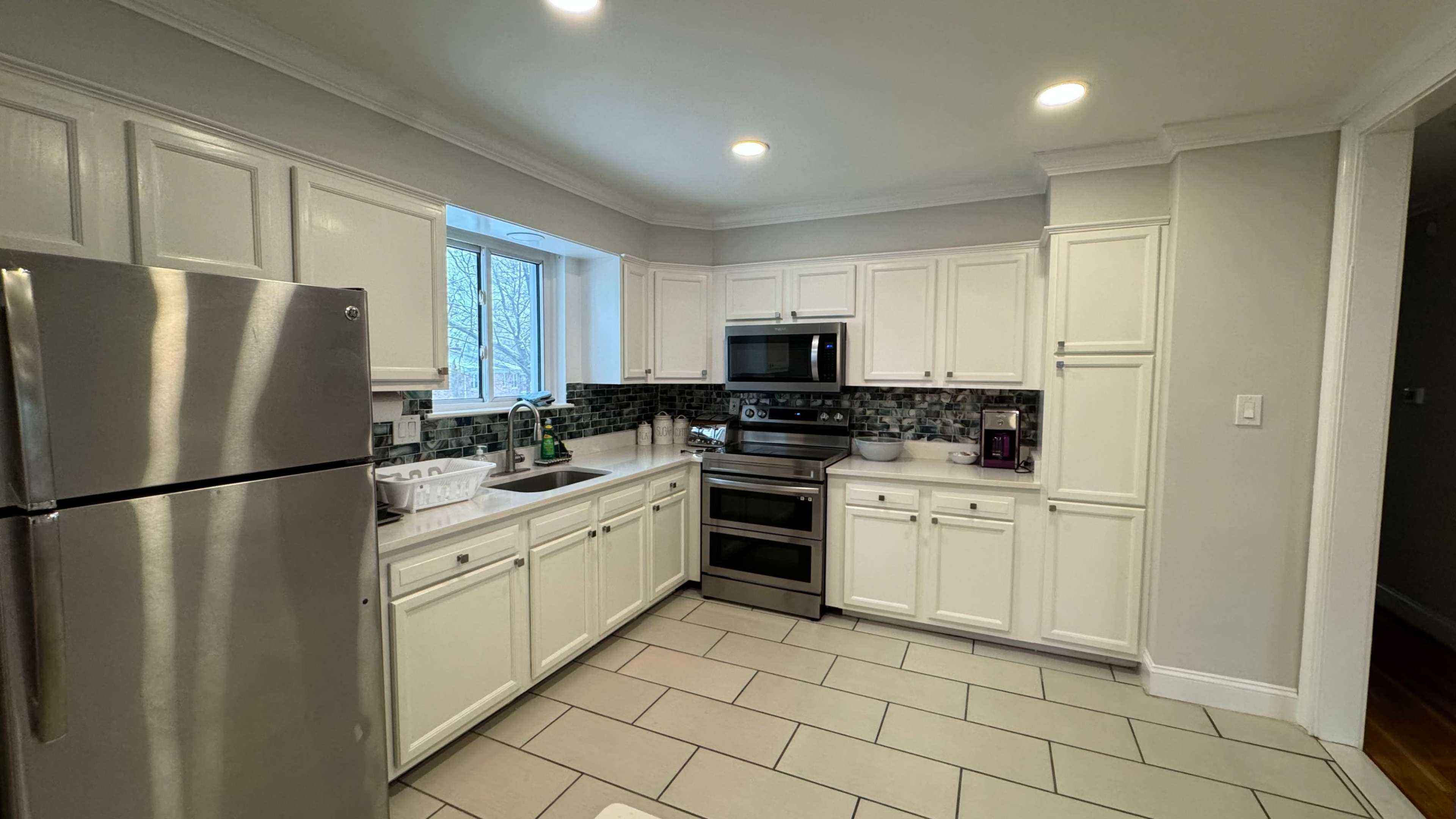 A modern kitchen featuring white cabinetry, stainless steel appliances, a central island, and tile flooring.