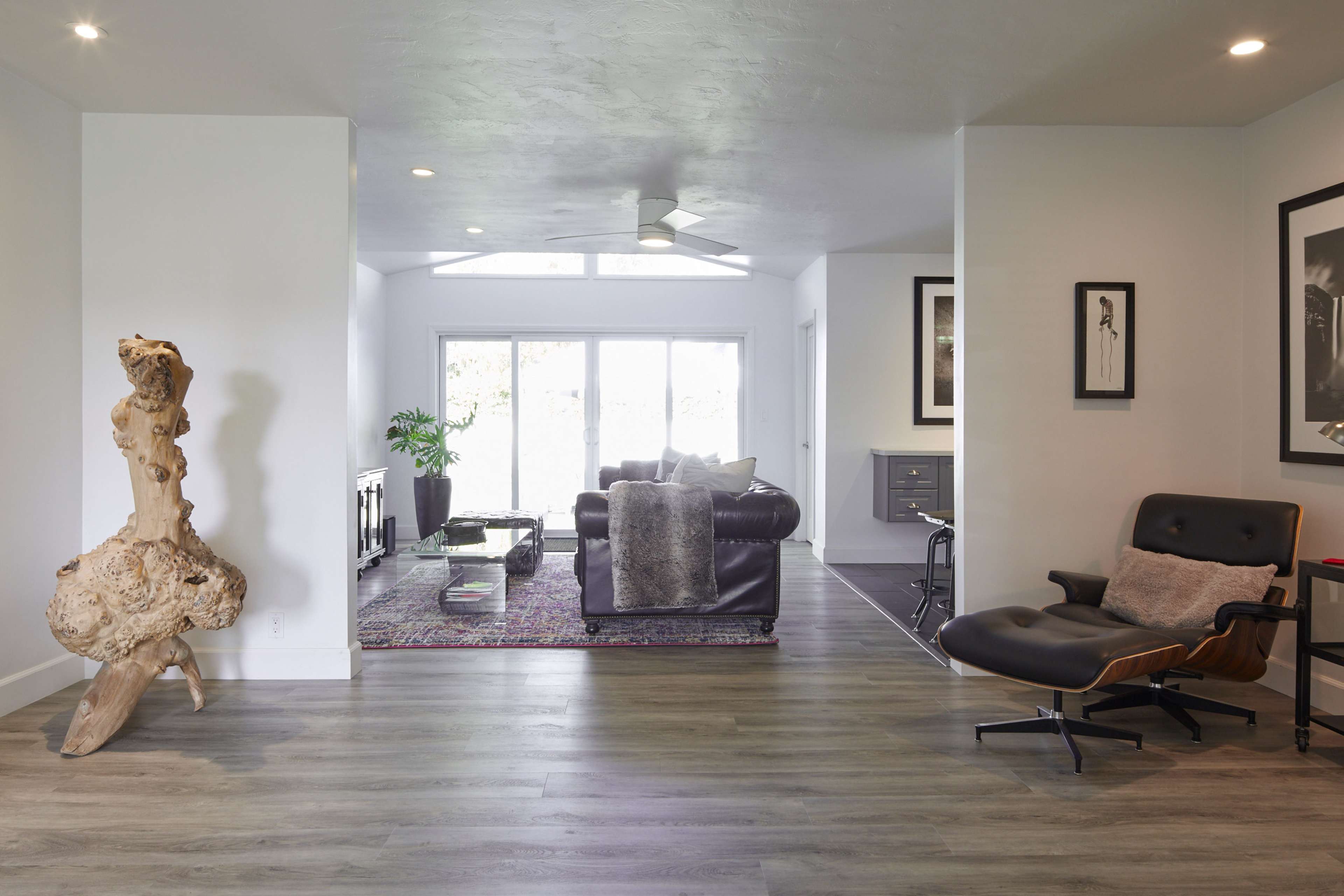 A spacious living area features a combination of modern furniture, a decorative wooden sculpture, and large windows that allow natural light to fill the room.