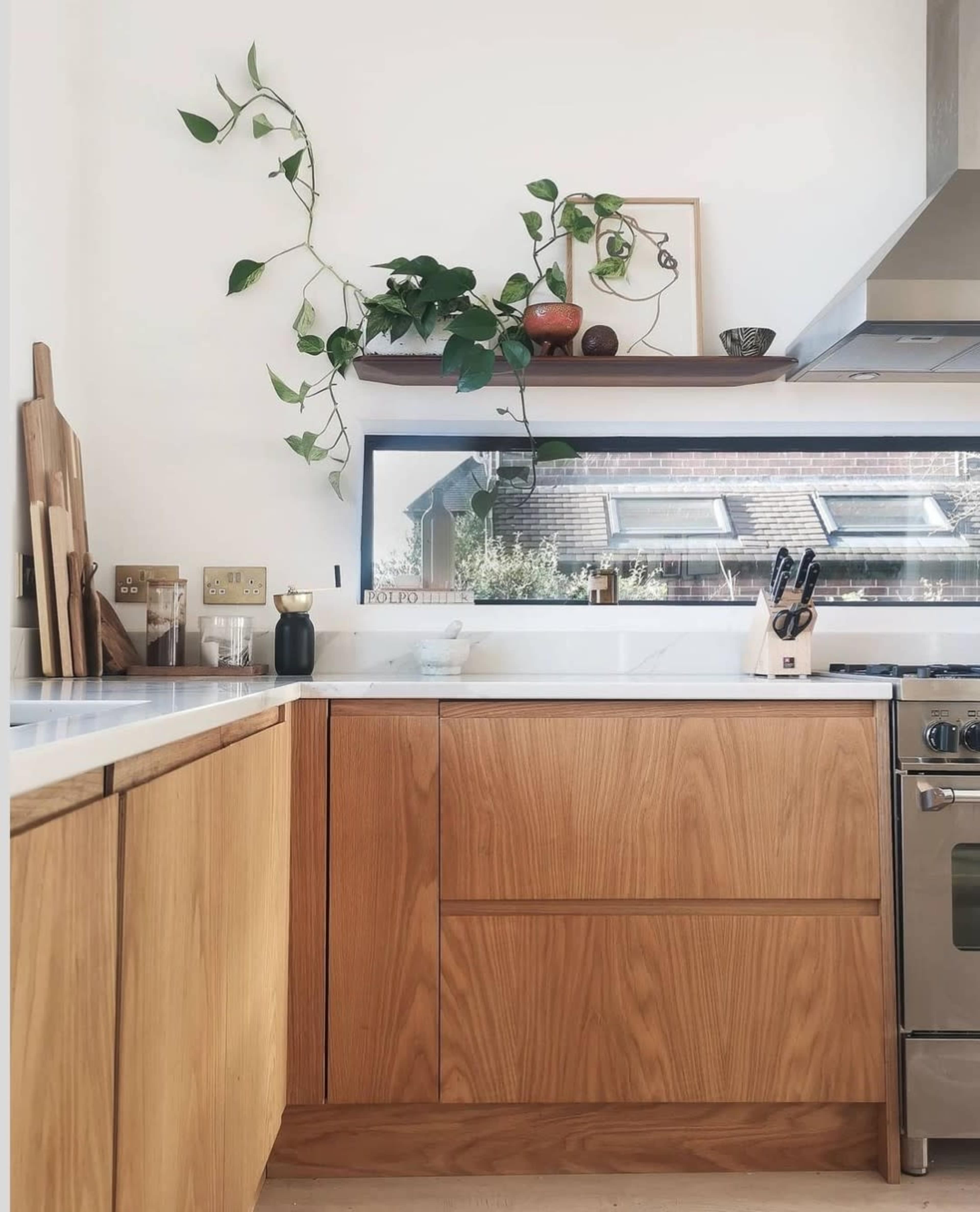 A modern kitchen features wooden cabinetry, a stainless steel stove, and a window with decorative plants above it.