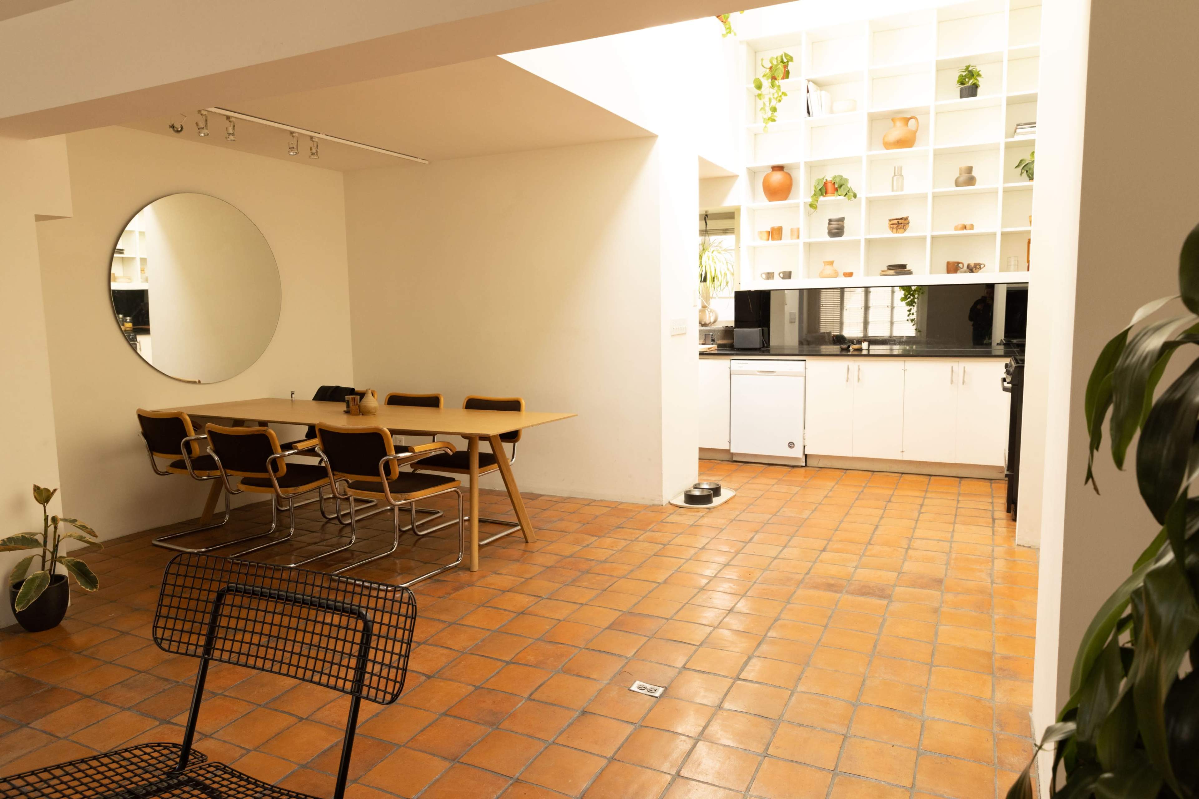 A spacious kitchen and dining area featuring a round mirror, a wooden table with seating, and a white cabinetry setup with a black countertop.