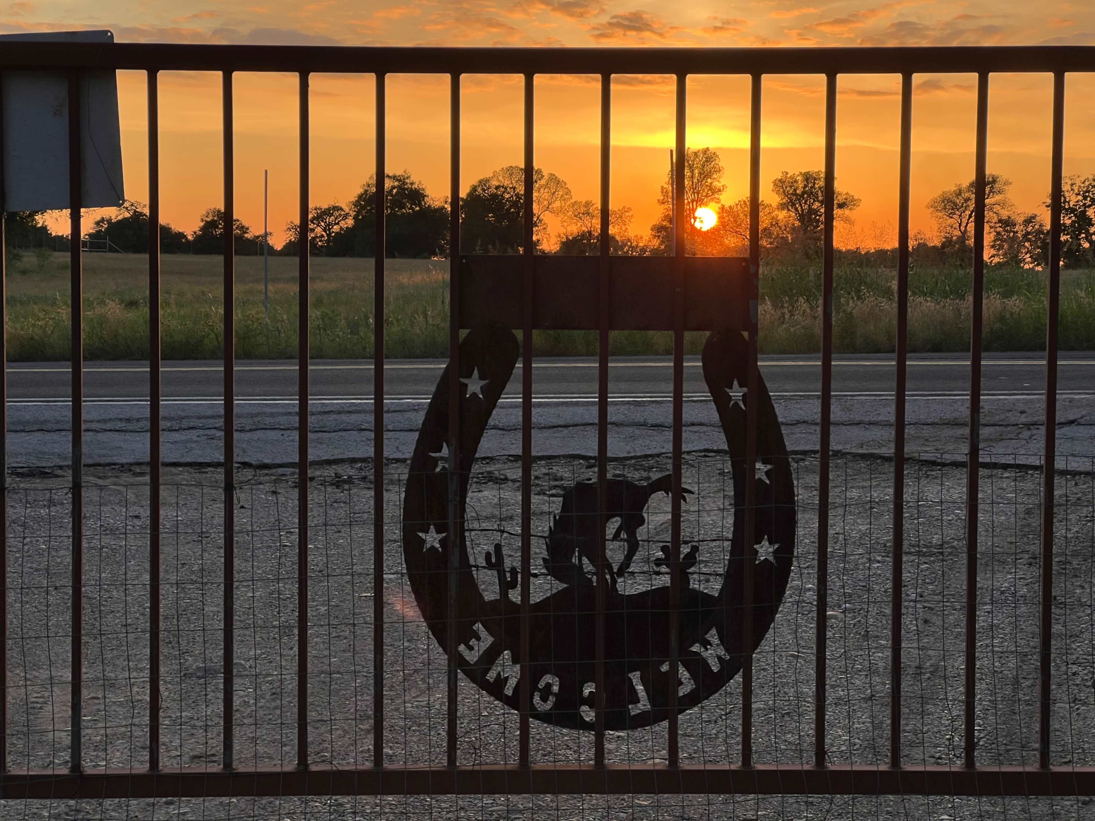 A metal gate shaped like a horseshoe displays the word "WELCOME" against the backdrop of a sunset.