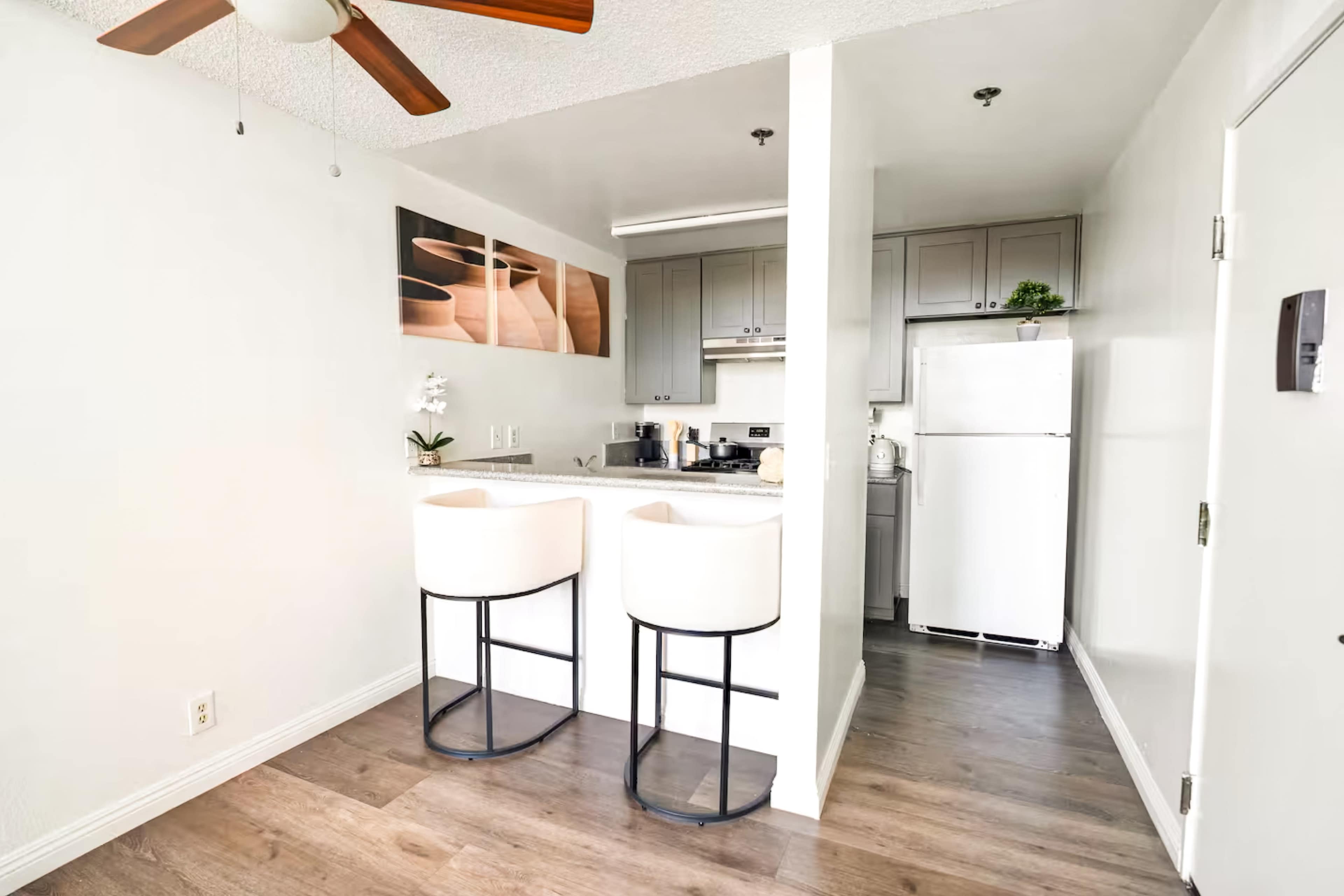 A modern kitchen features a breakfast bar with two white stools, grey cabinets, and stainless steel appliances.