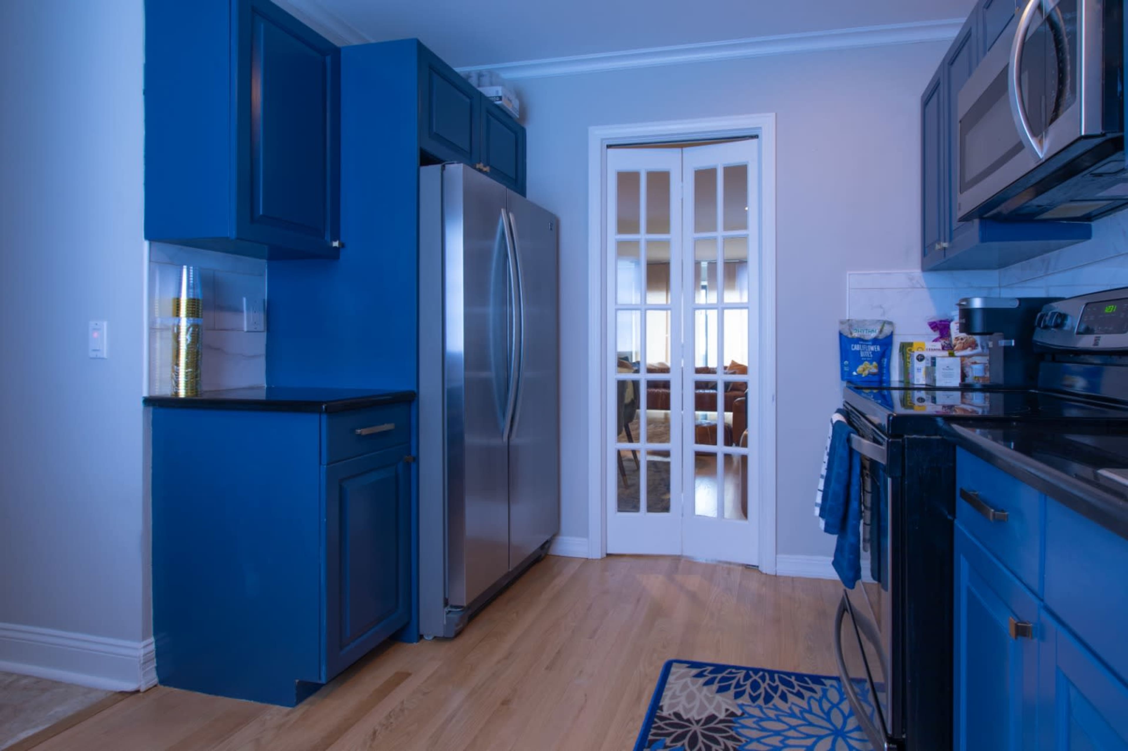 A modern kitchen features blue cabinetry, stainless steel appliances, and a view into a adjacent room through a set of glass doors.