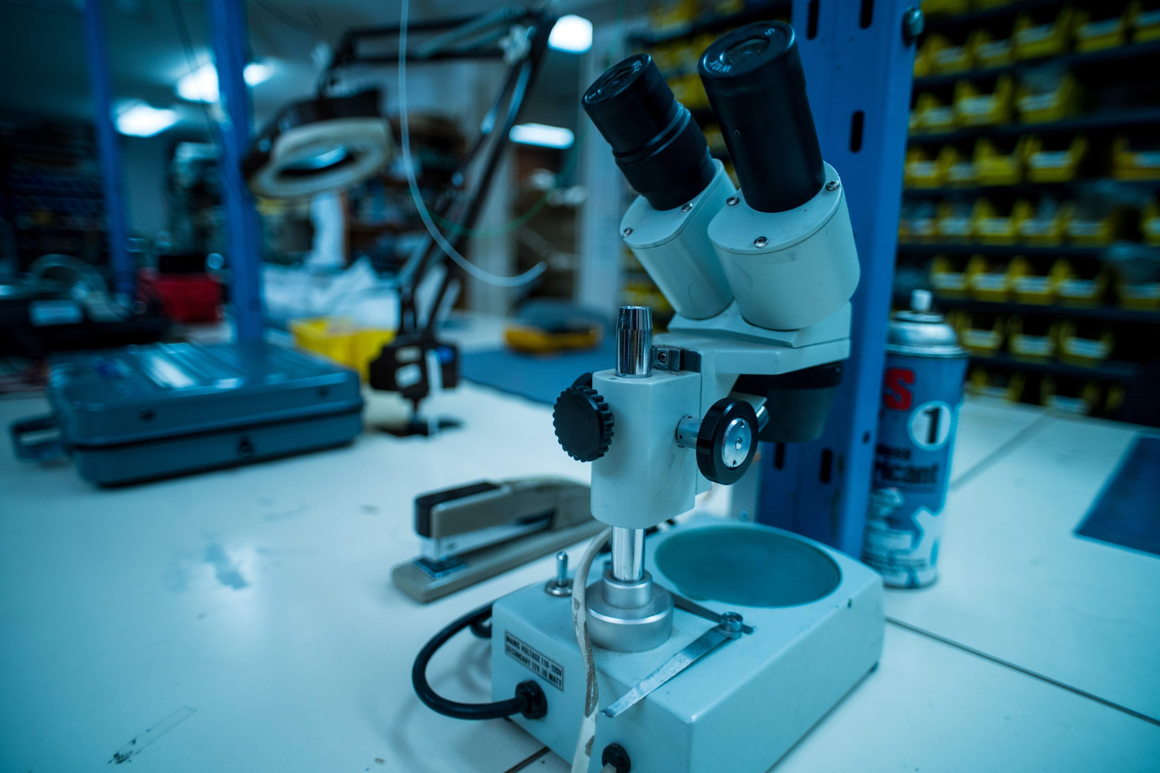 A laboratory workbench with a microscope, various tools, and a can of aerosol spray in the background.
