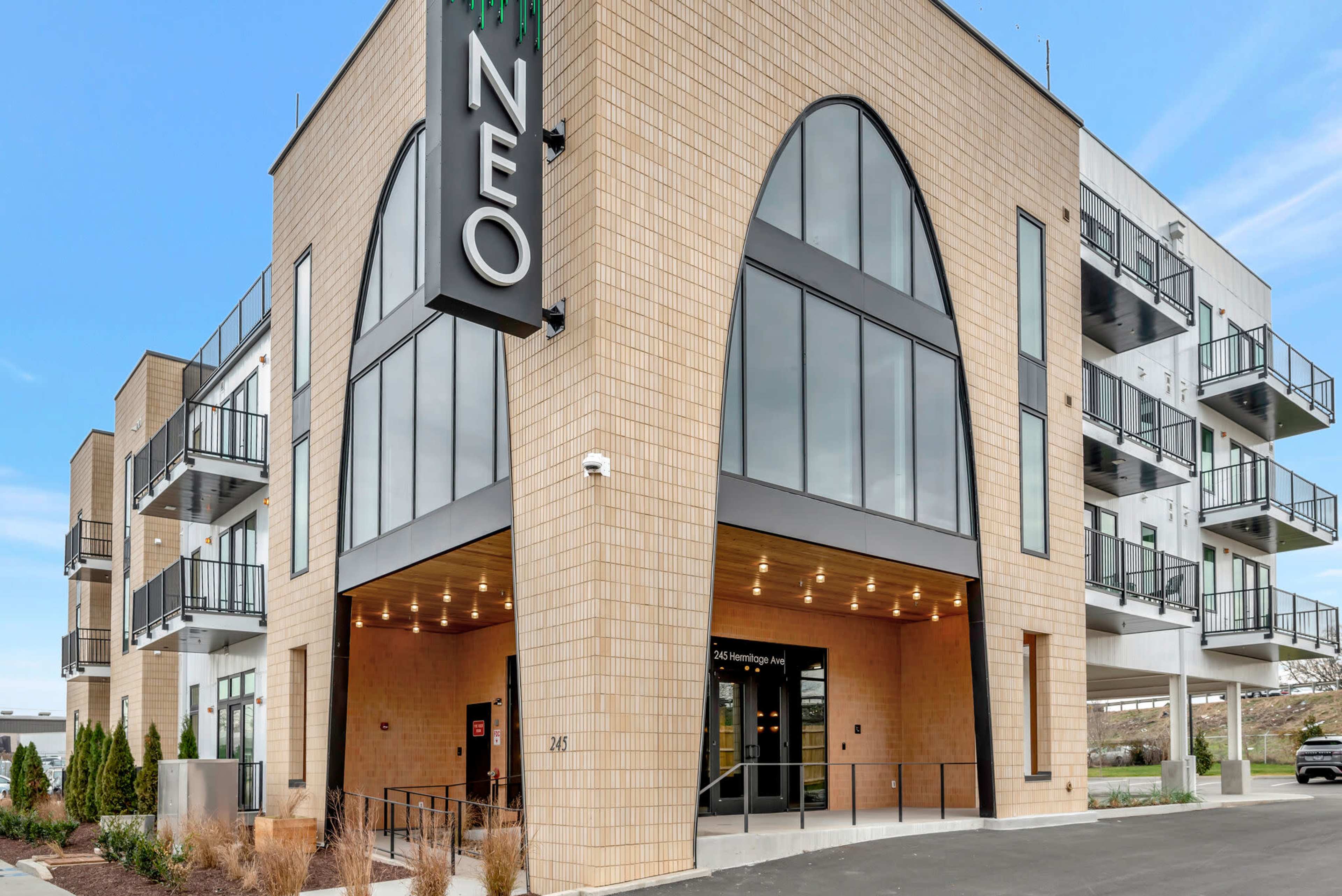 A modern multi-story building features large arched windows and a prominent entrance with the name "NEO" displayed above.
