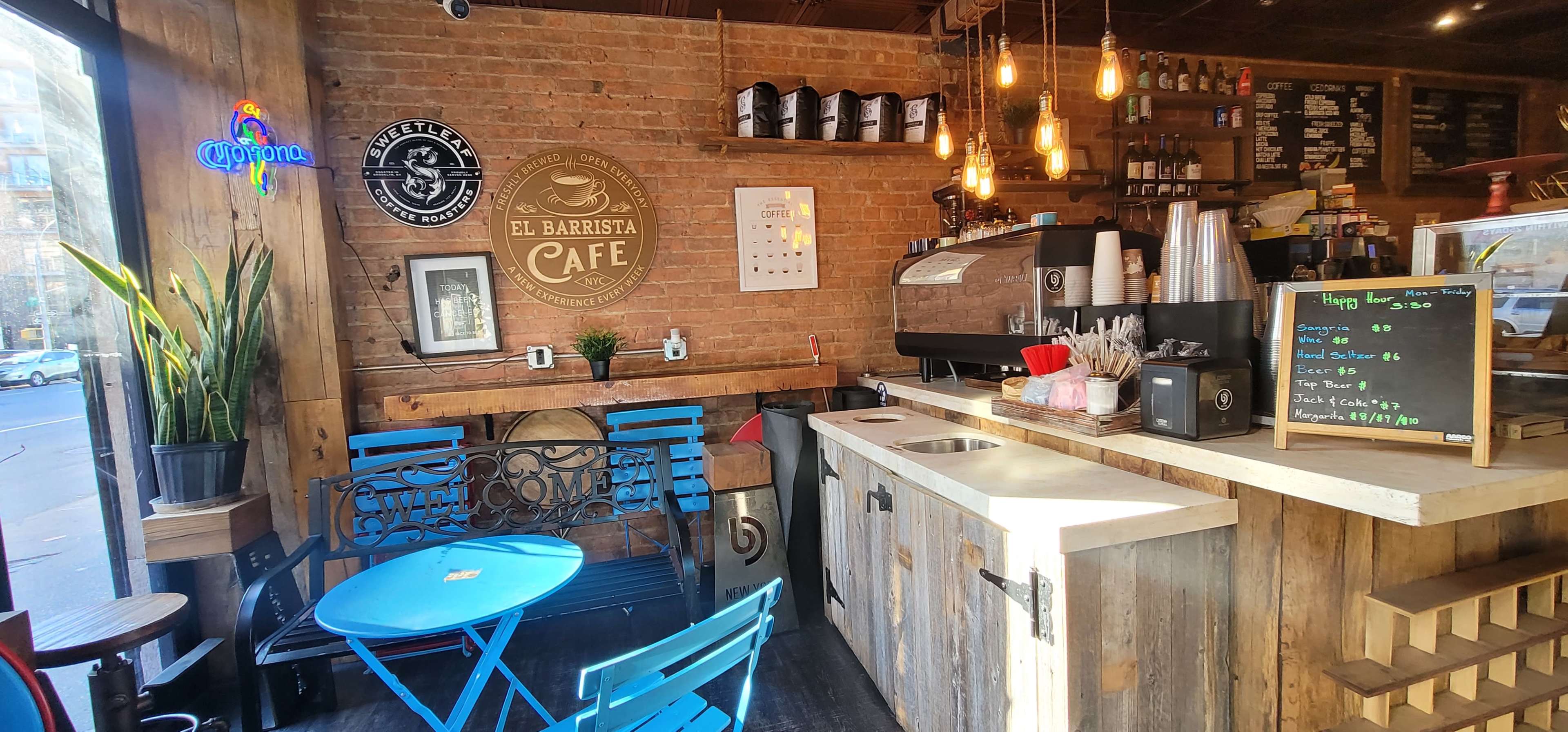 A cozy coffee shop features a brick wall, wooden counter, and blue tables with chairs near a coffee machine and menu board.
