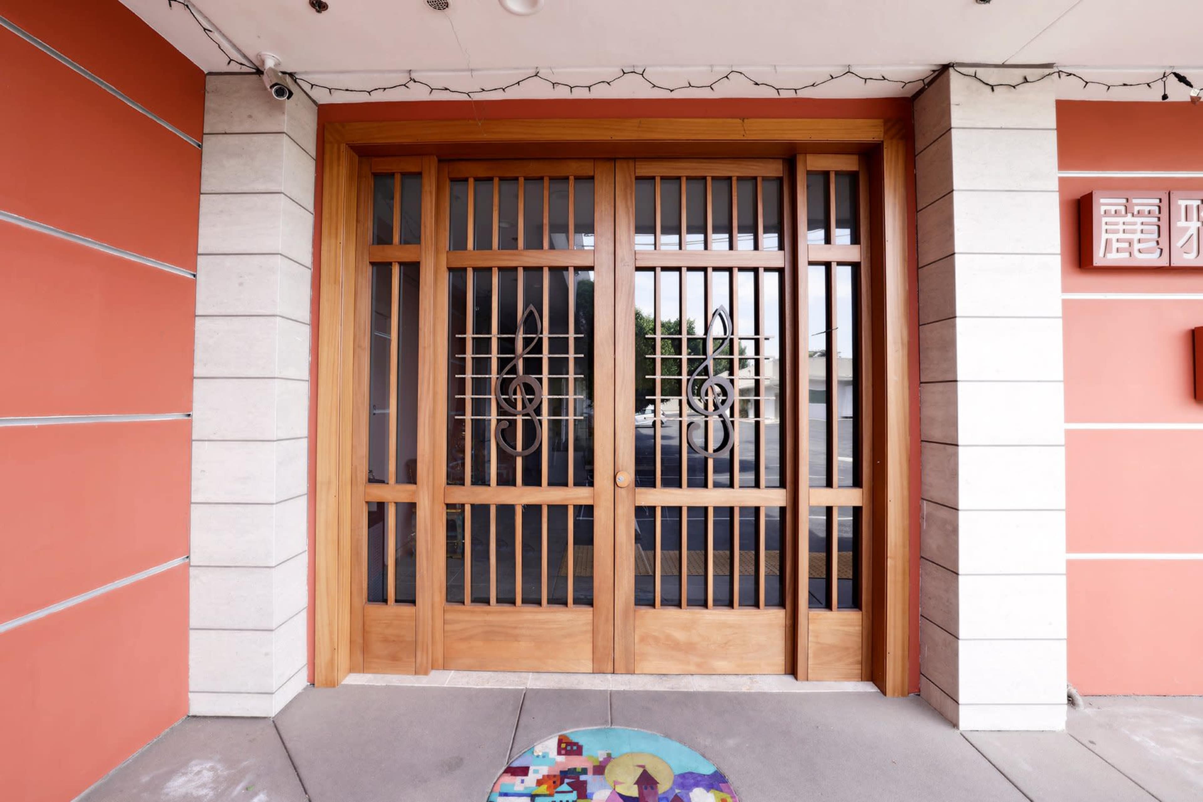 A wooden double door with decorative music note designs, set within a building that has orange walls and stone accents.