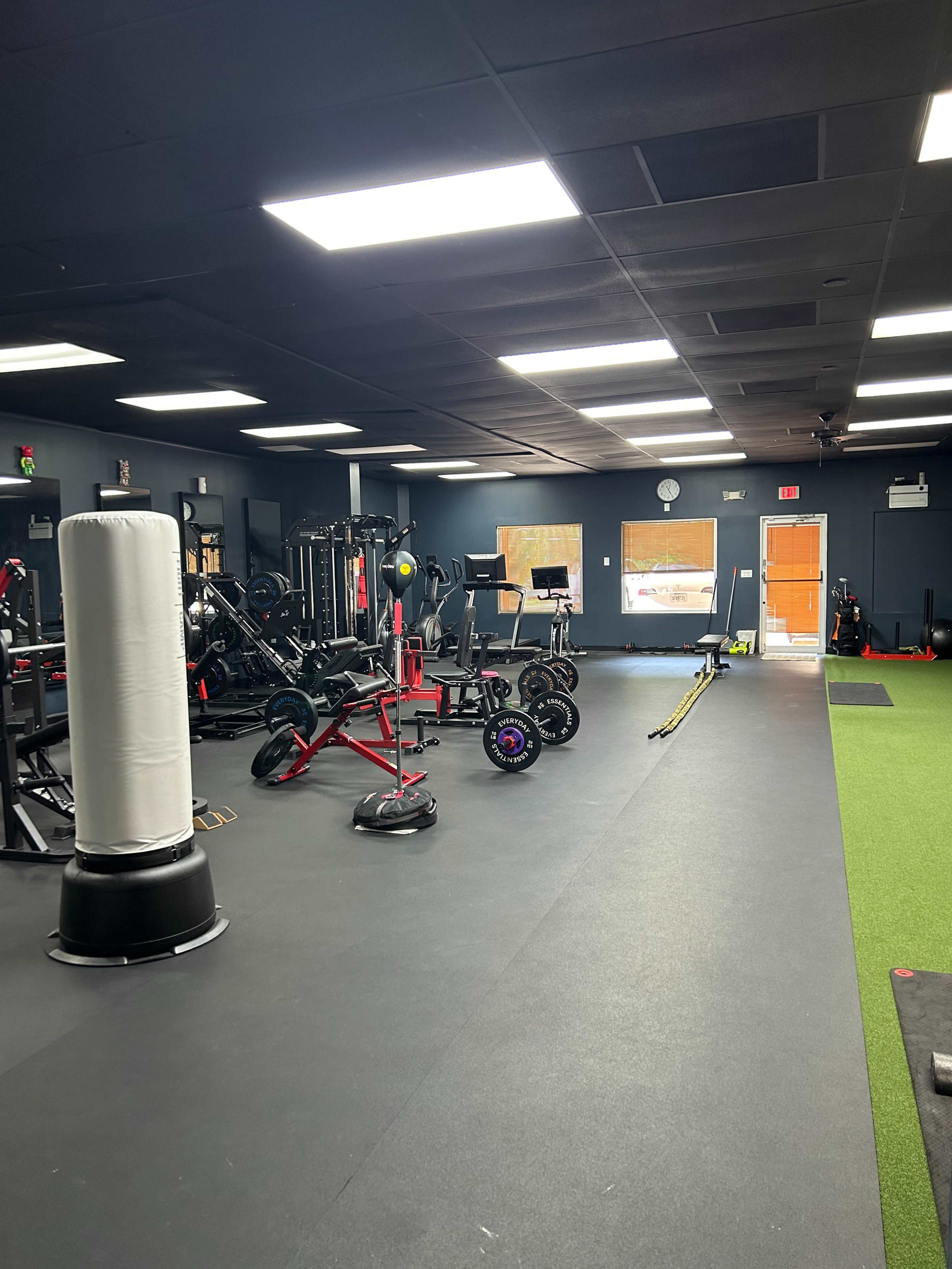 A gym interior with various fitness equipment, including weights, mats, and a punching bag, under bright overhead lights.
