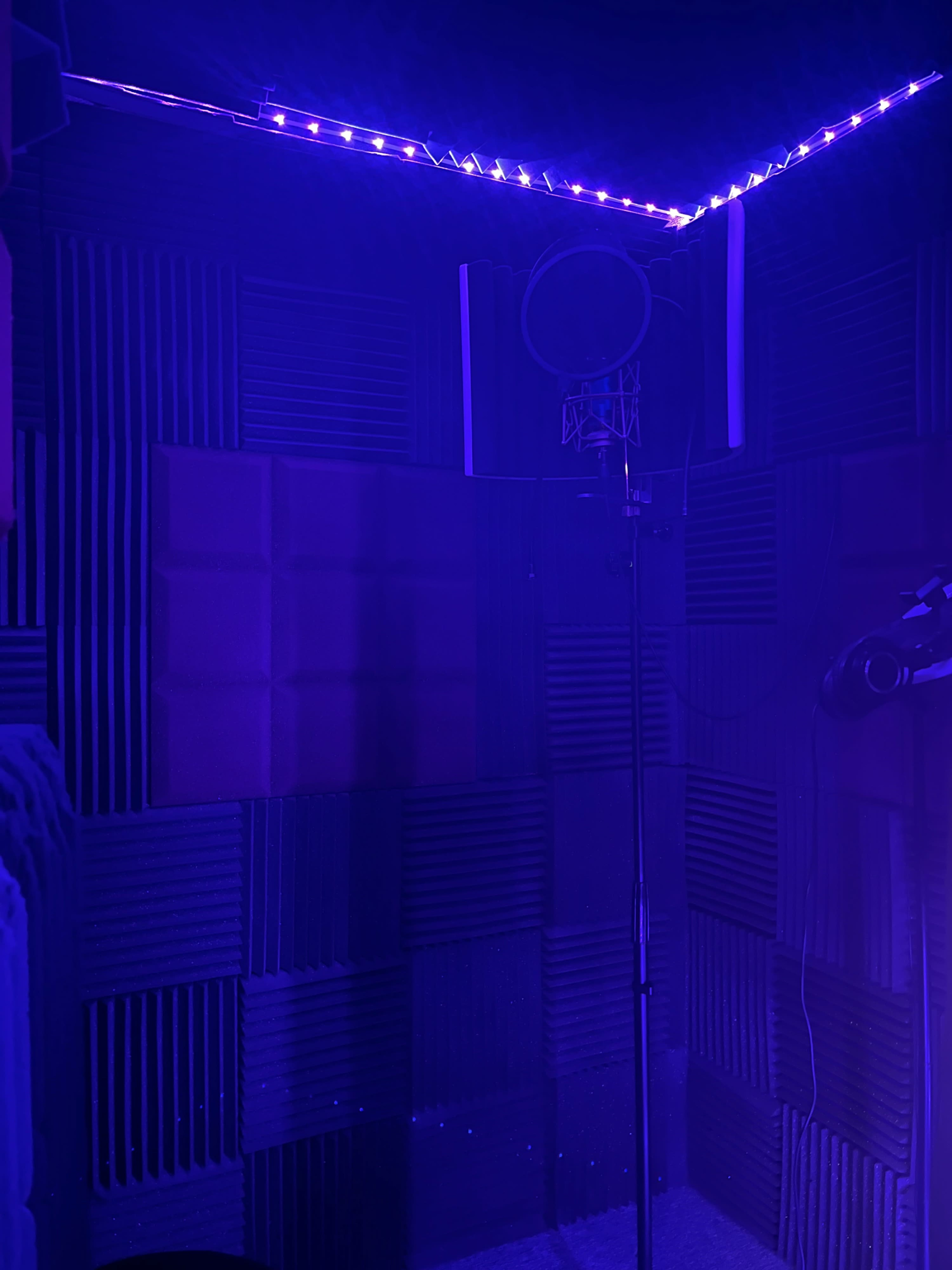 A soundproof recording booth with acoustic foam panels and a microphone stand illuminated by purple LED lights.