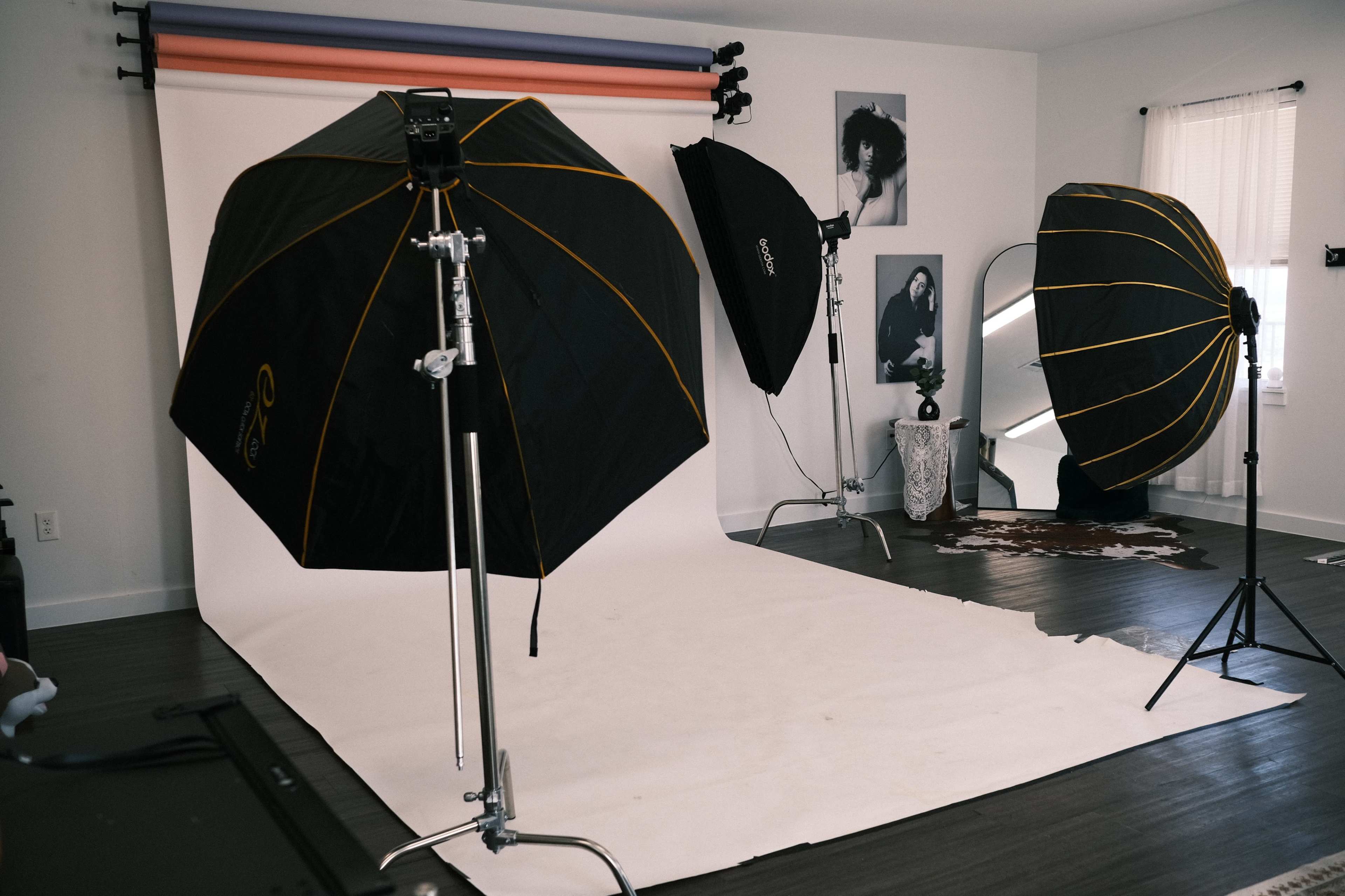 The image shows a photography studio setup with multiple light umbrellas, a backdrop, and a large white floor area.