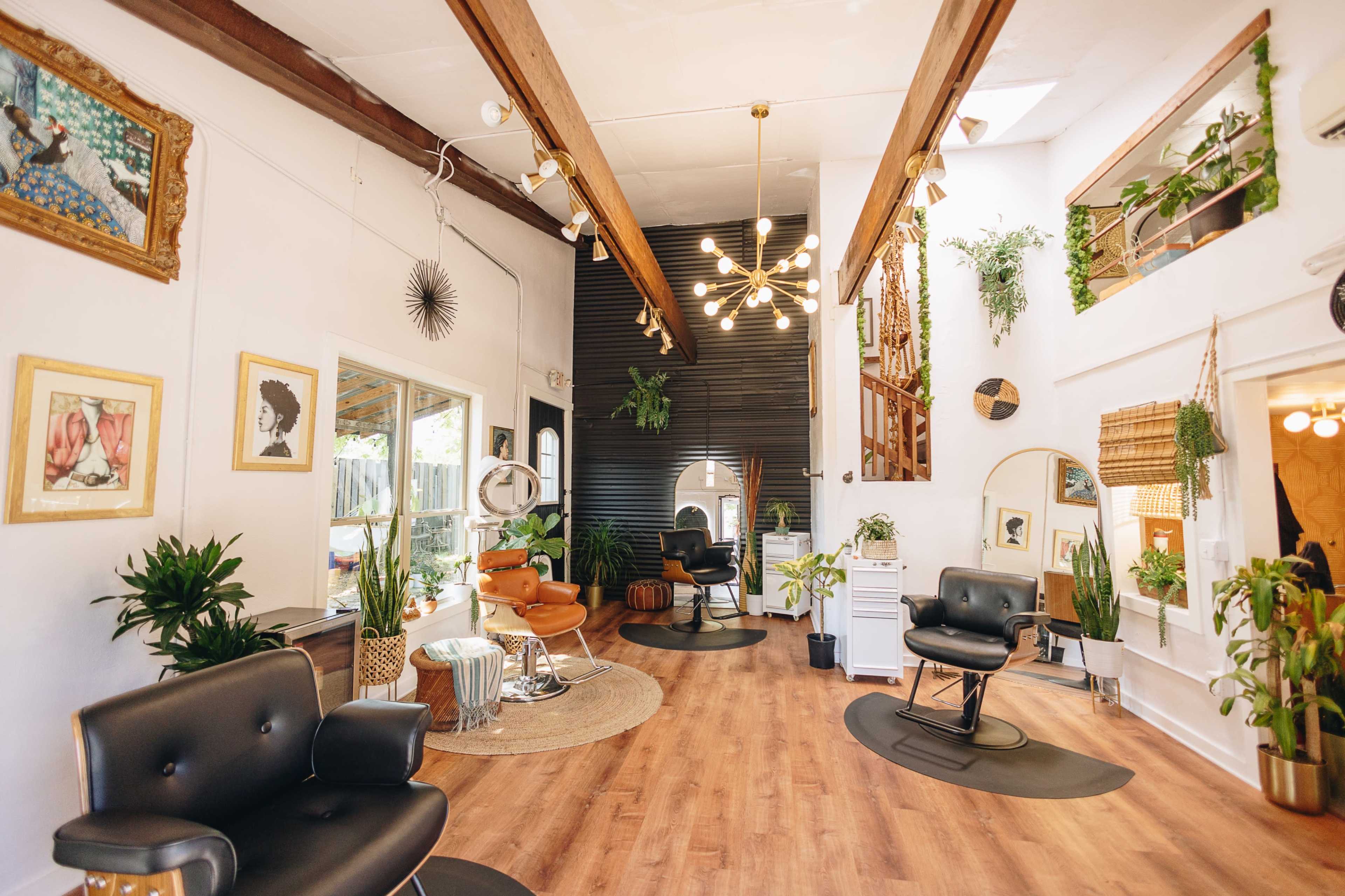 A well-lit salon featuring modern styling chairs, wooden beams, and a variety of indoor plants.
