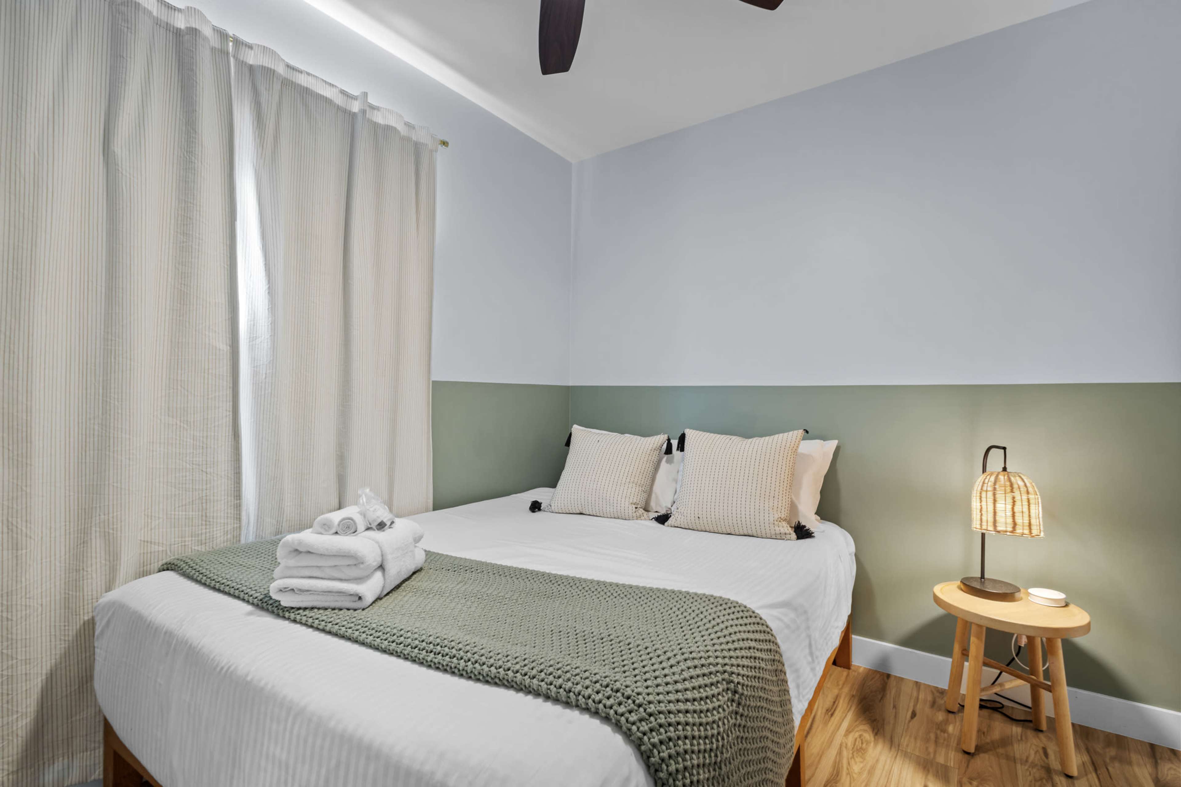 A cozy bedroom features a double bed with white linens, a green throw blanket, and a small bedside table with a lamp.