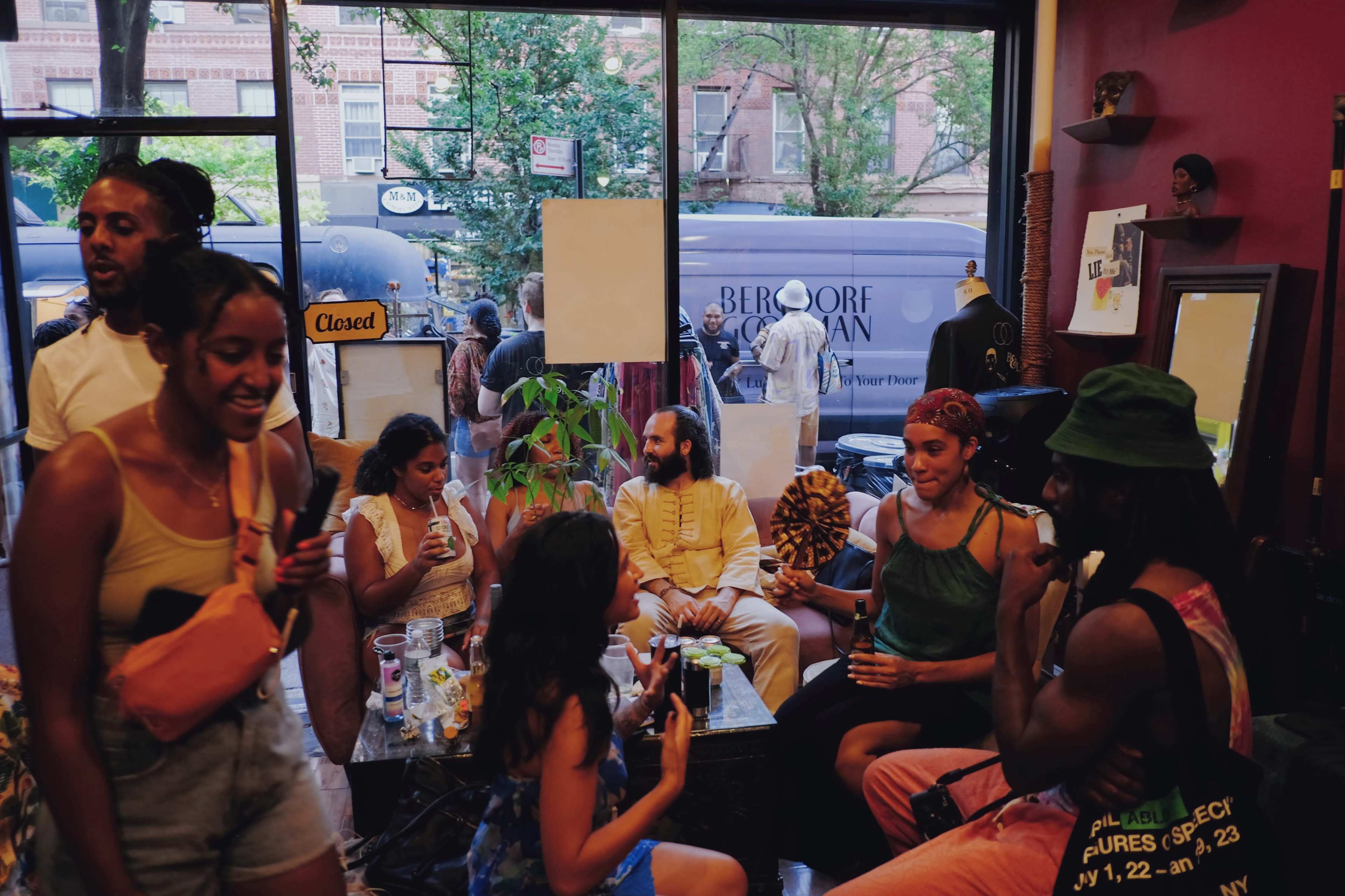 A group of people socializes inside a boutique, while others can be seen outside through the window.