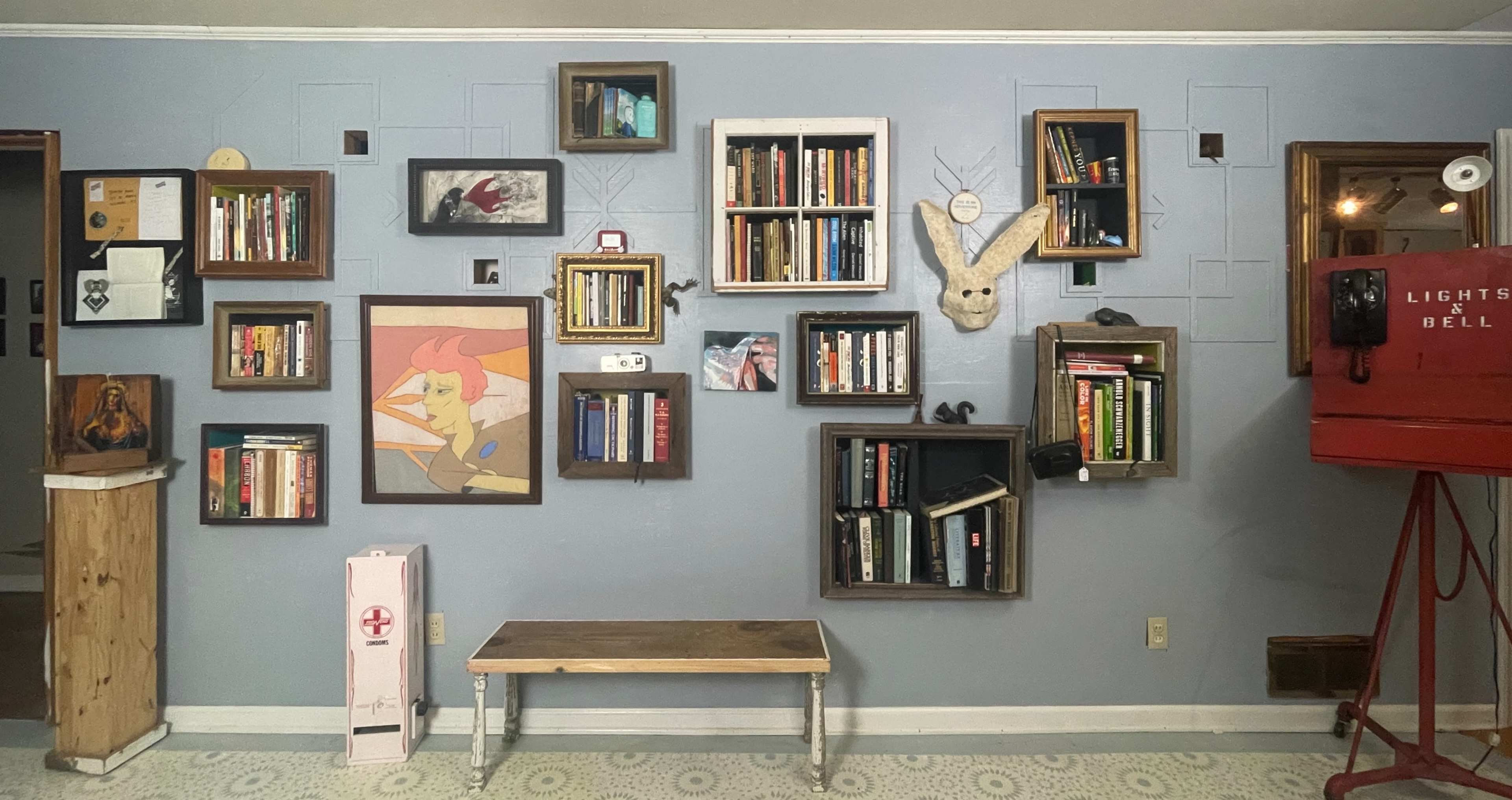 The image shows a wall with a variety of bookshelves arranged in a geometric pattern, featuring books, artwork, and a decorative animal head.