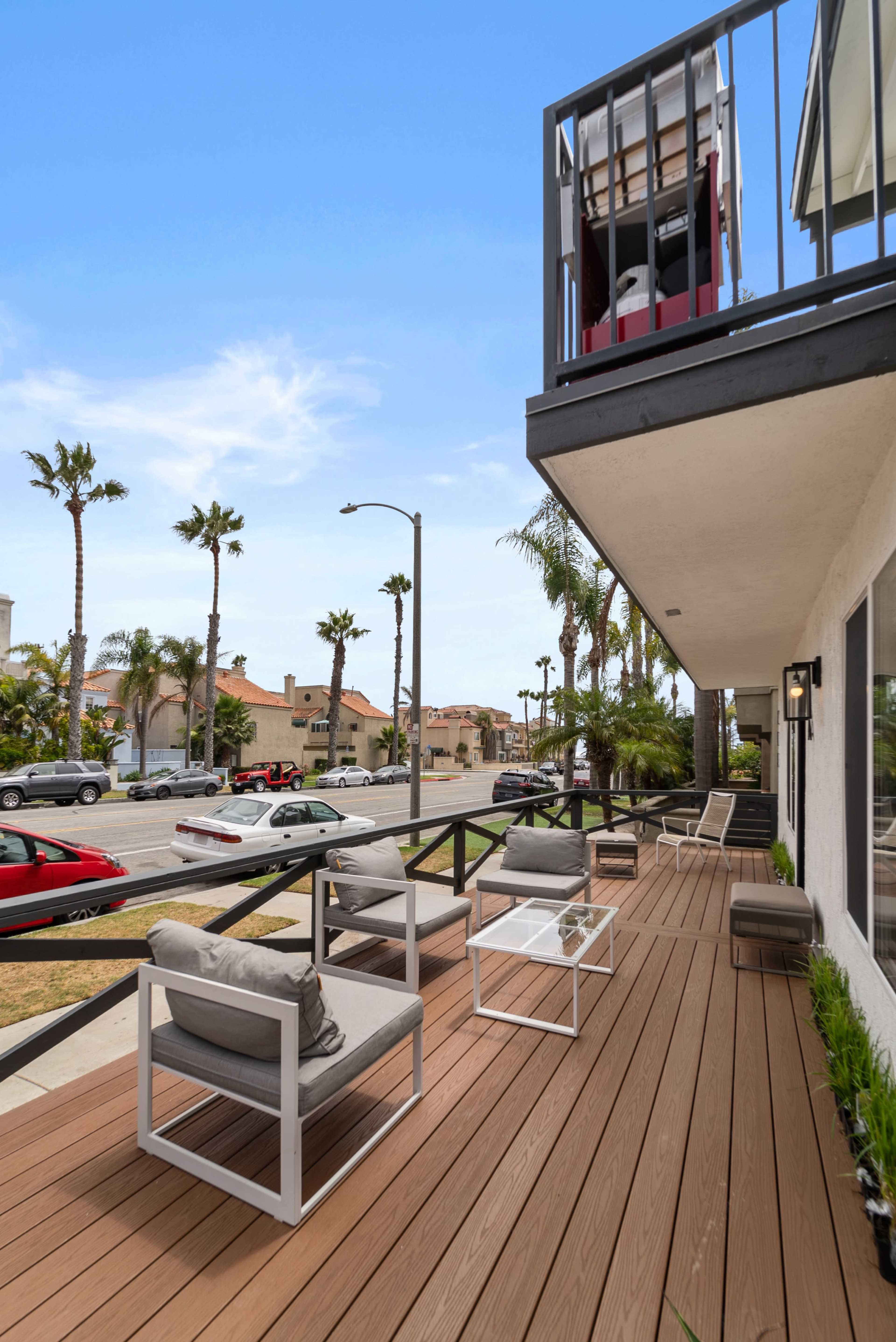 A modern deck with seating overlooks a street lined with palm trees and residential buildings.