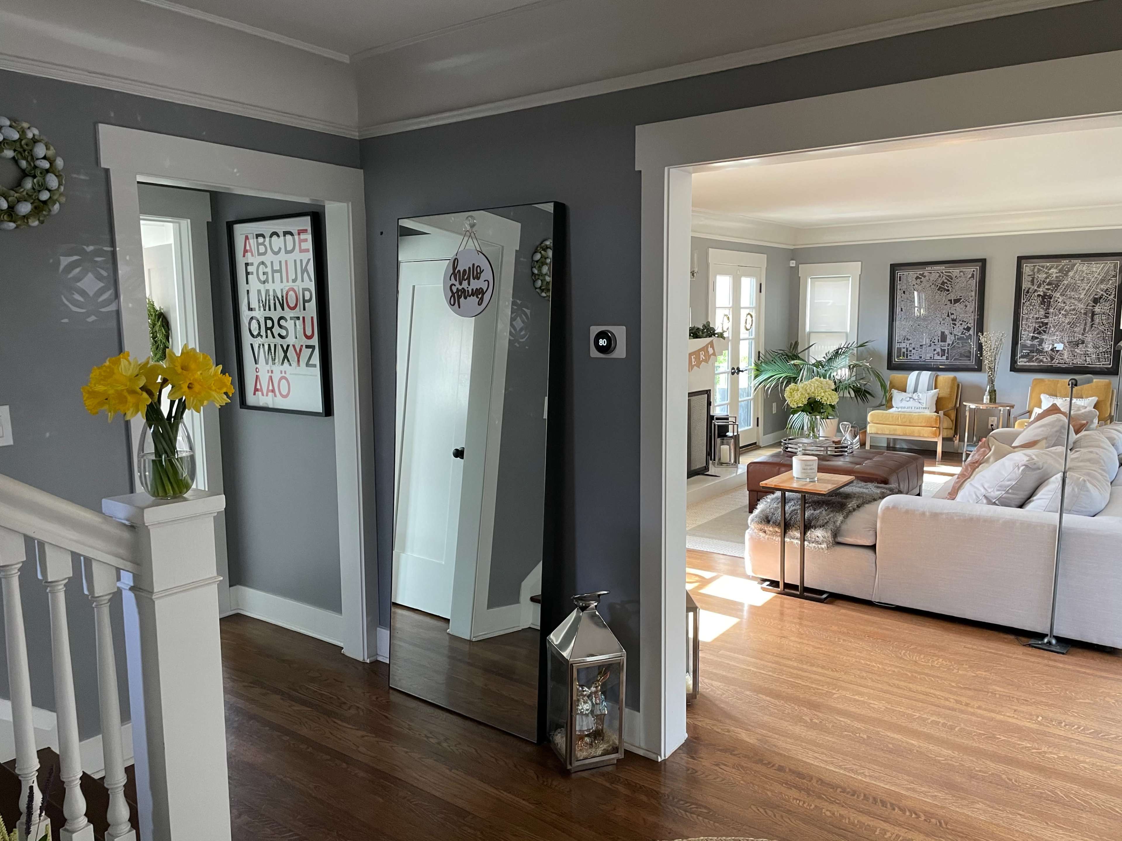A well-lit interior space with a hallway leading to a living room featuring a sofa, decorative plants, and framed artwork on the walls.