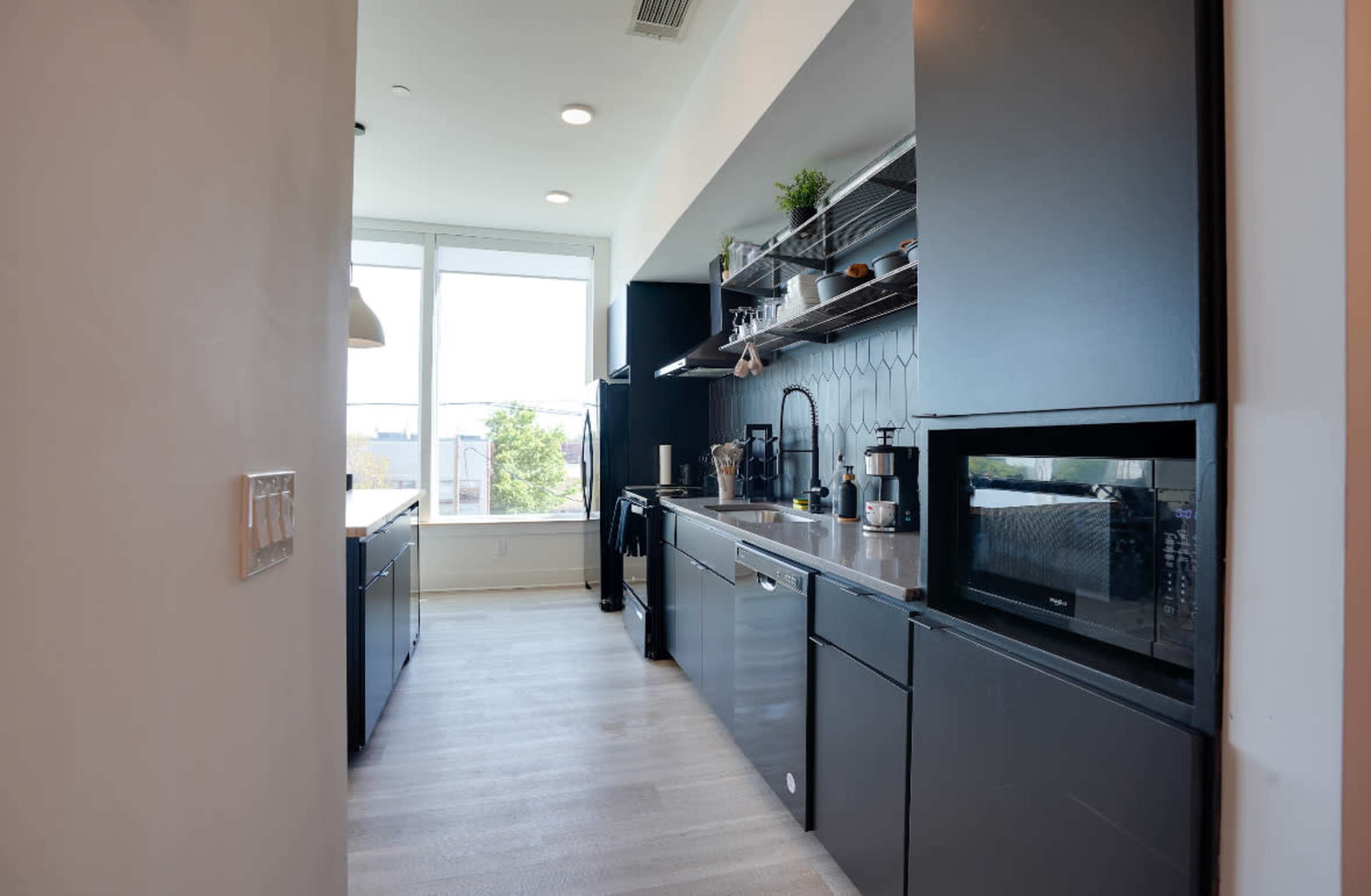 A modern kitchen with sleek black cabinets, stainless steel appliances, and a window providing natural light.