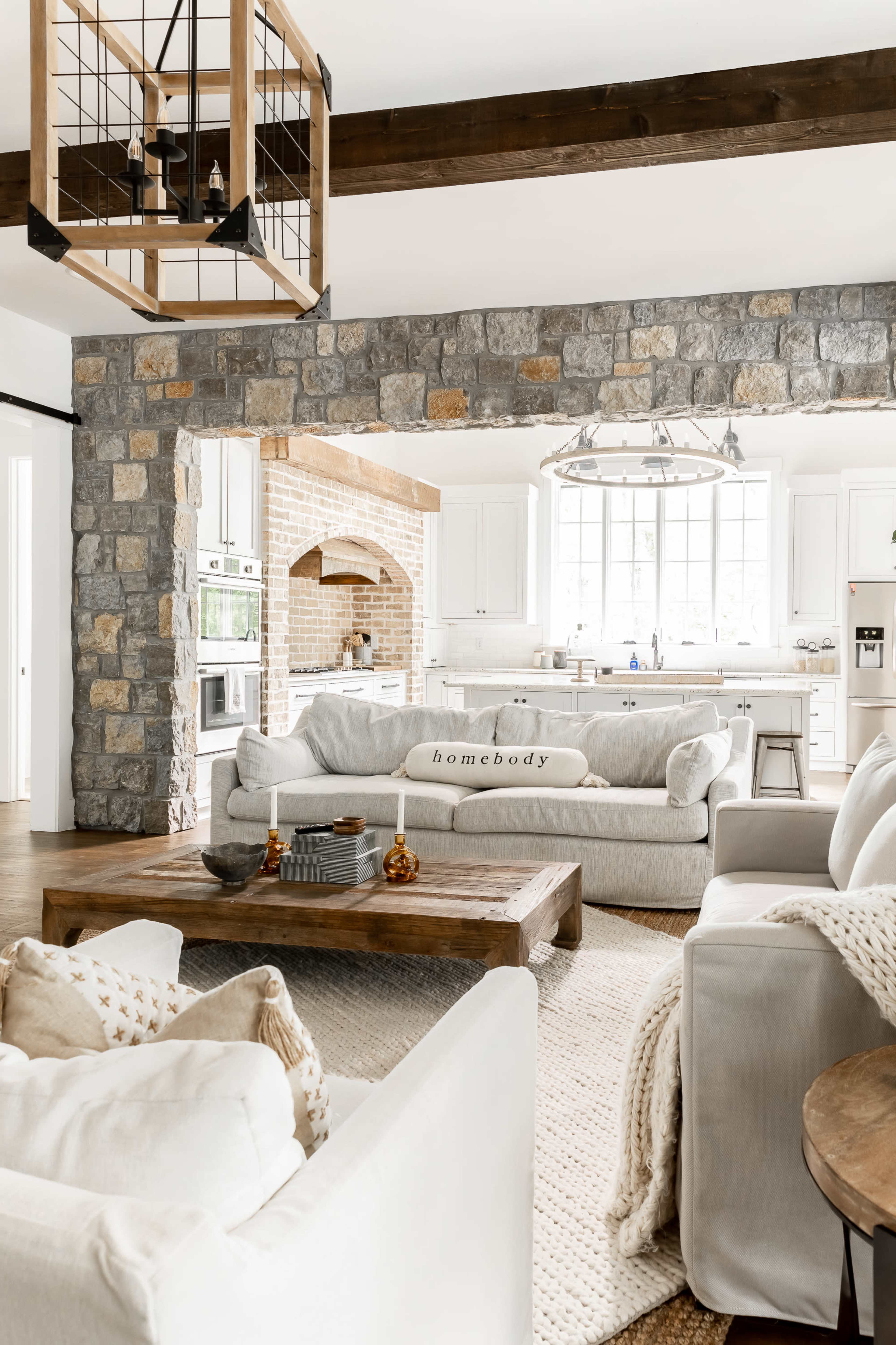 A modern kitchen and living area with a stone archway, featuring a soft gray sofa, a wooden coffee table, and a bright, open layout with large windows.