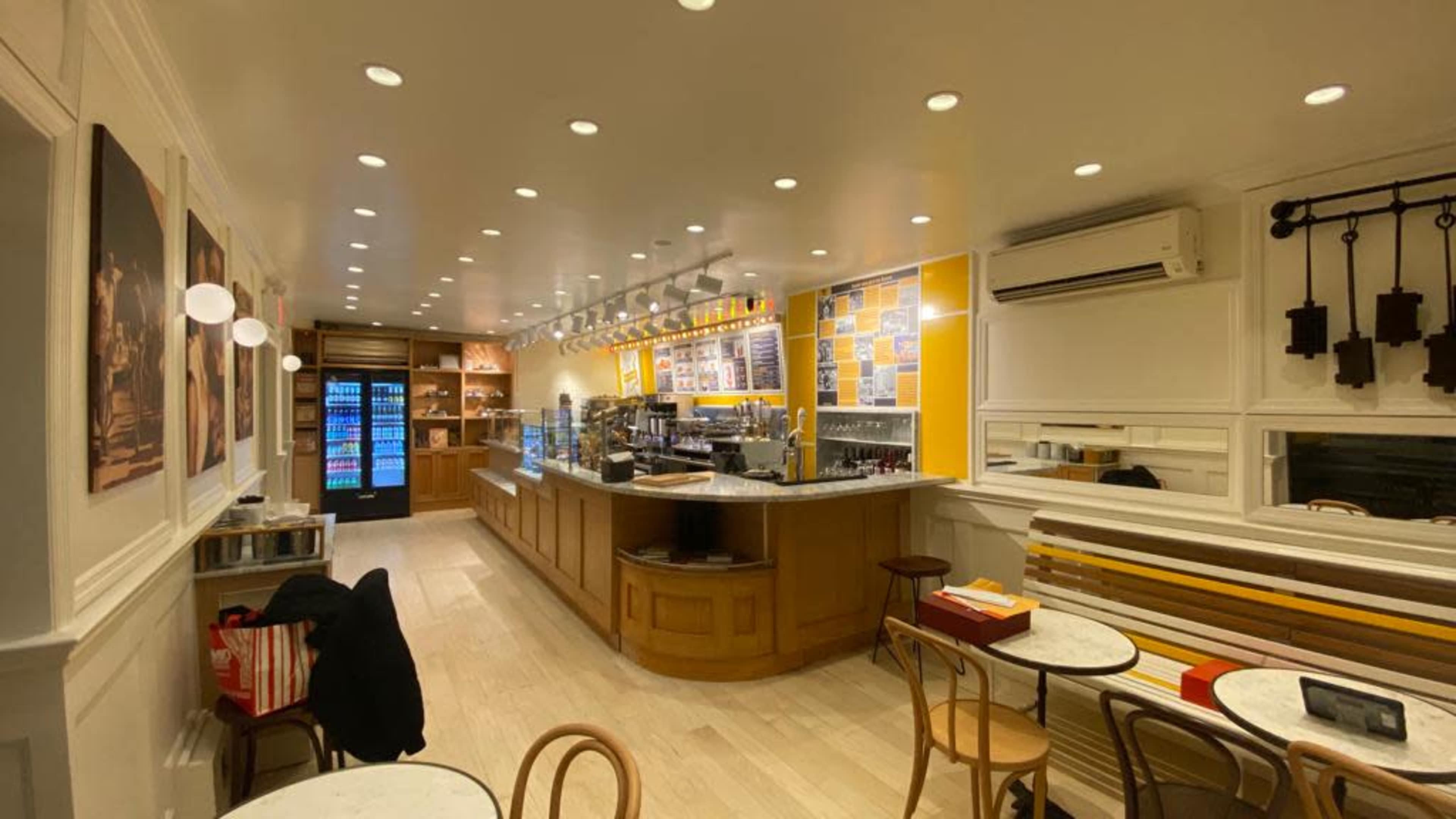 The image shows a modern café interior with a long counter, a display case, and seating arrangements, featuring bright lighting and minimalistic decor.