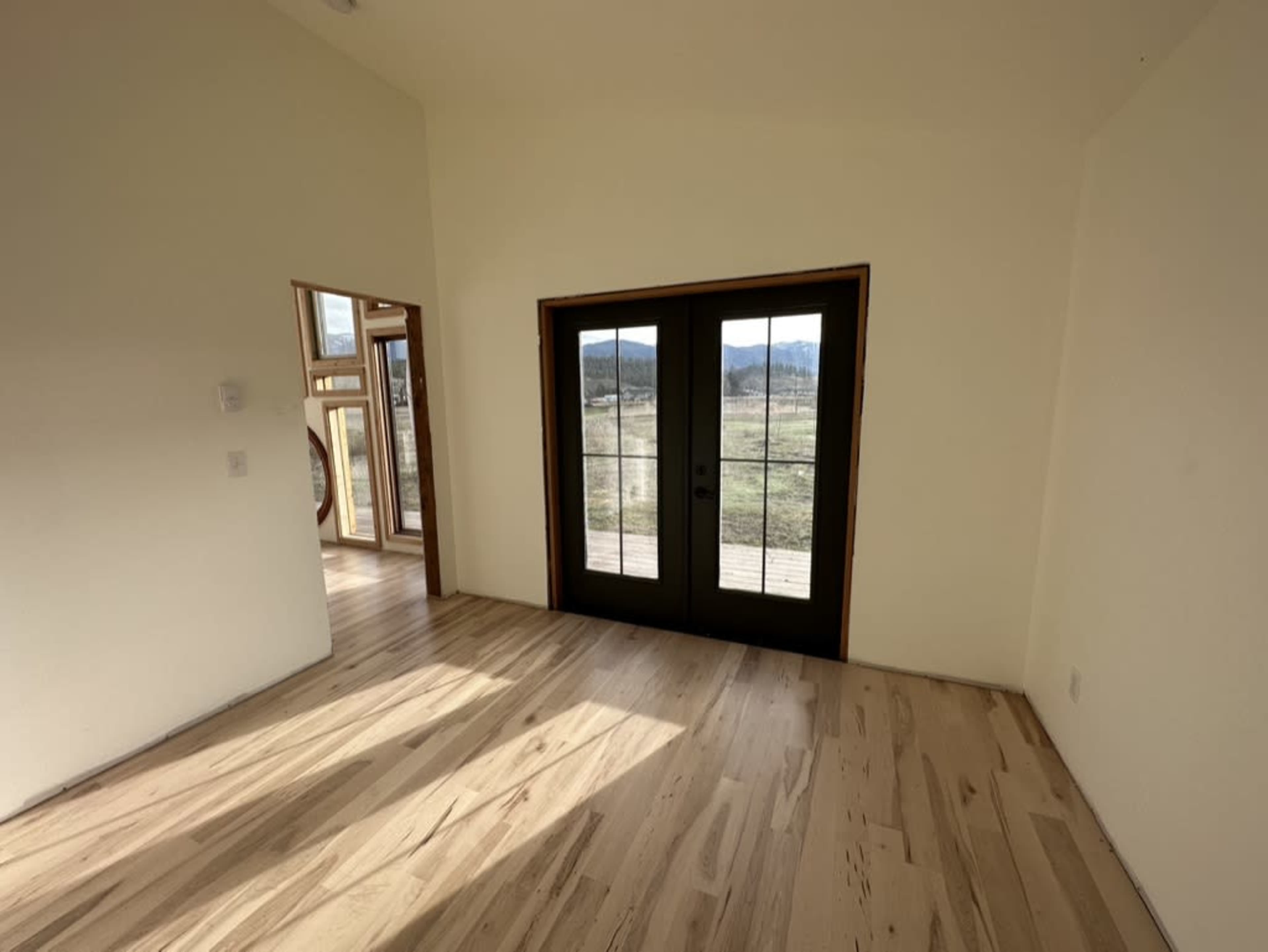 The room features a wooden floor and a set of black French doors leading to an outdoor area with a view of the landscape.