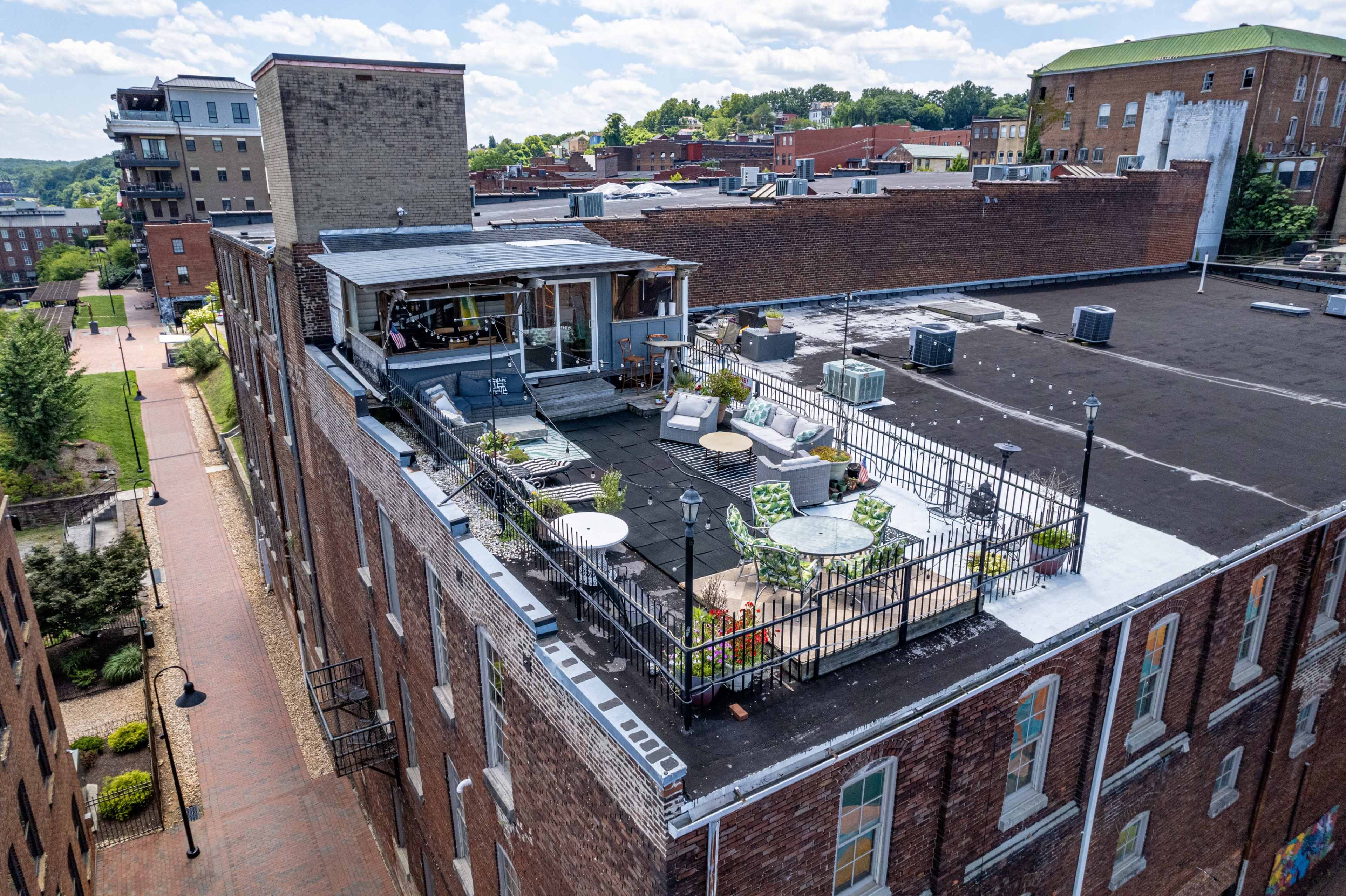 A rooftop terrace with various seating arrangements and plants atop a multi-story brick building in a city.