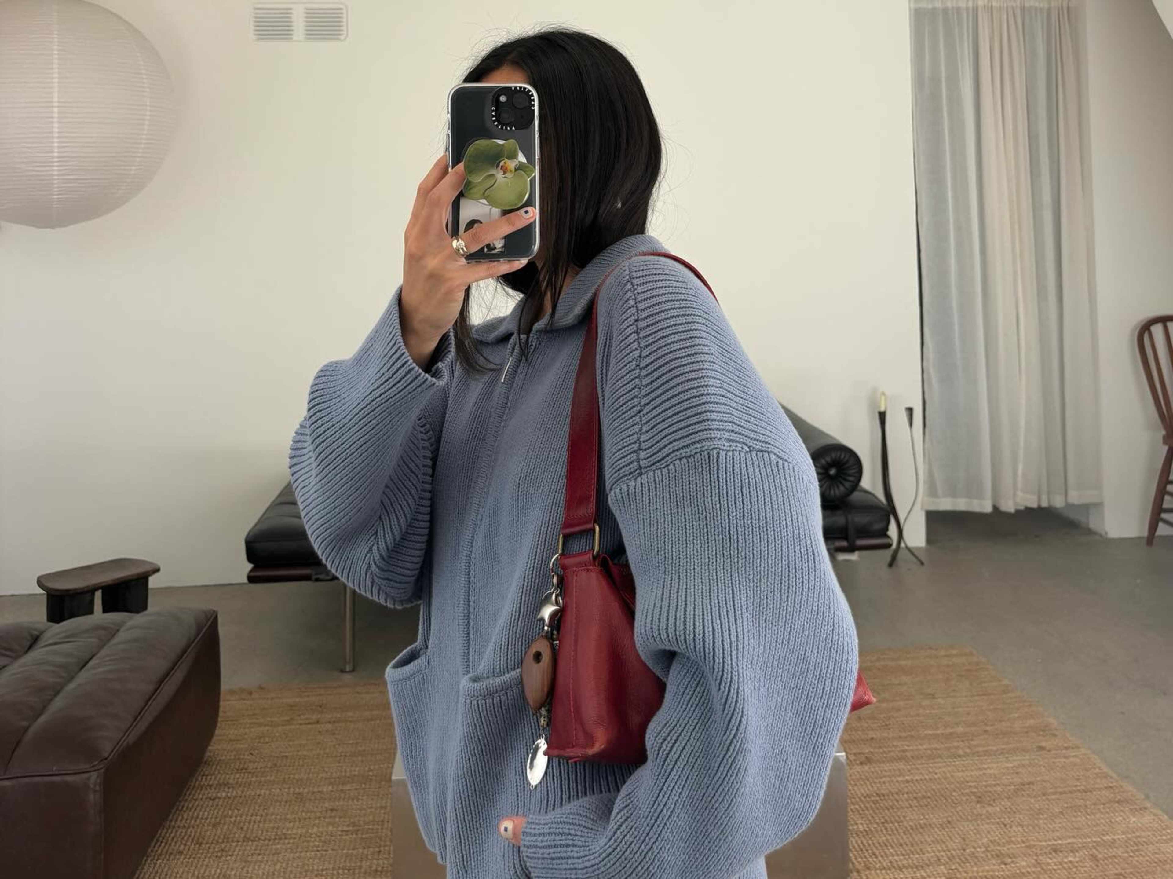 A person wearing a blue hoodie poses for a photo in a room with minimalist décor.