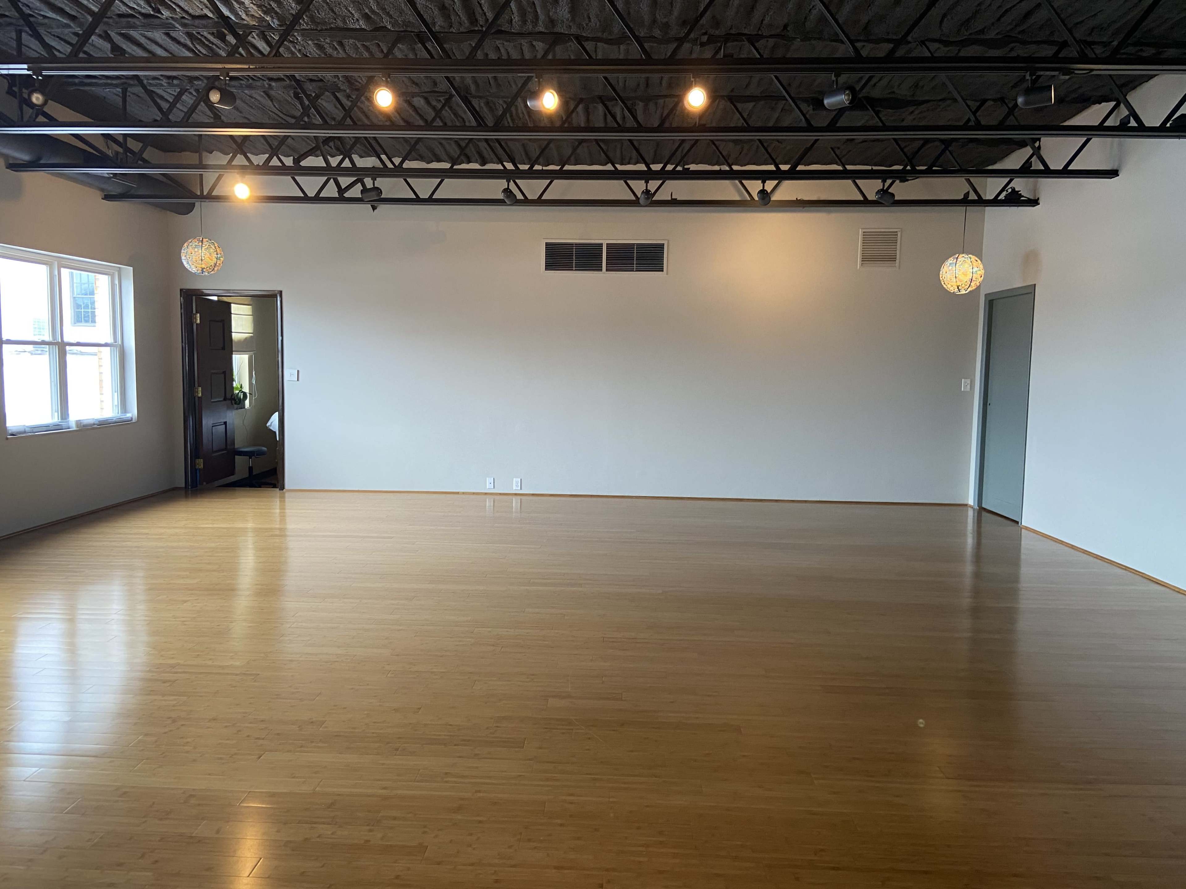 A spacious room with bamboo flooring, a high ceiling supported by exposed beams, and two spherical light fixtures hanging above.