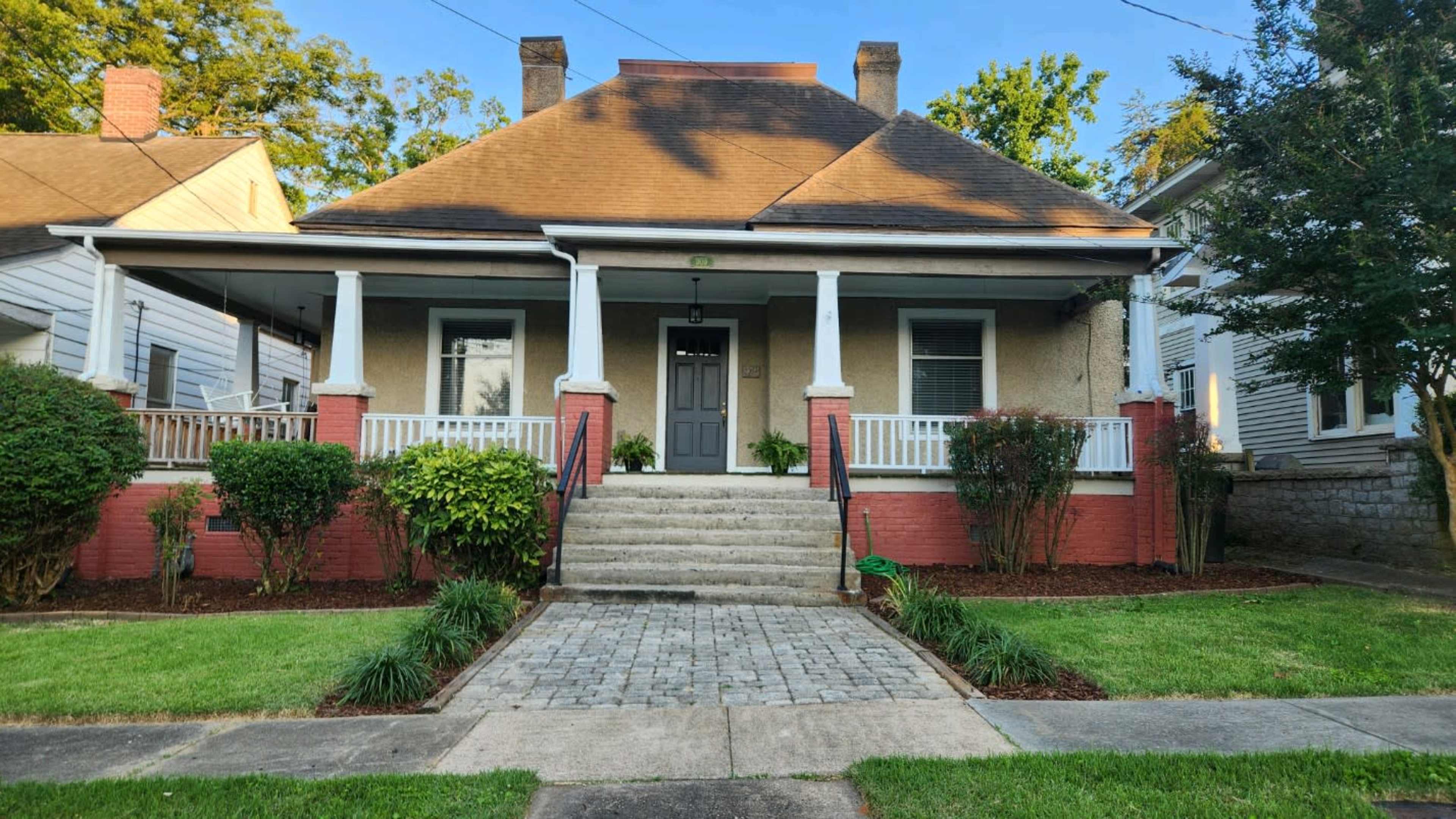 The image shows a single-story house with a spacious front porch, stone steps, and a landscaped yard.