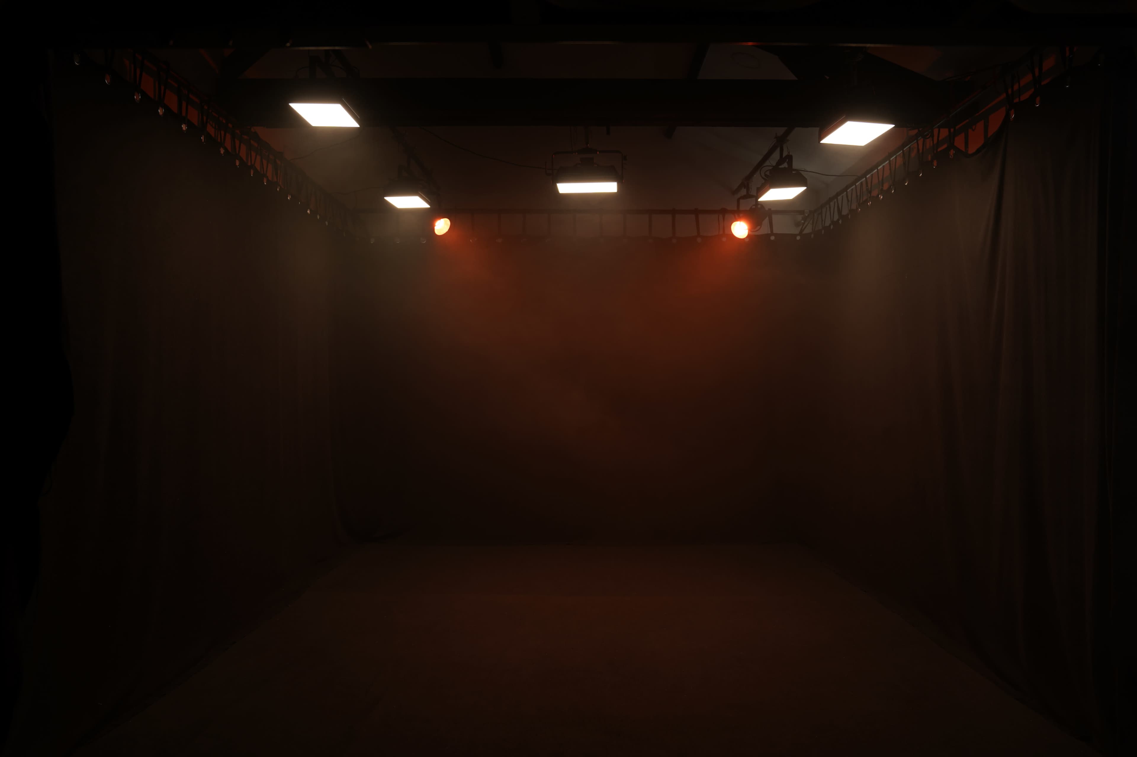 A dimly lit stage enclosed by black curtains, with red lights illuminating the center.
