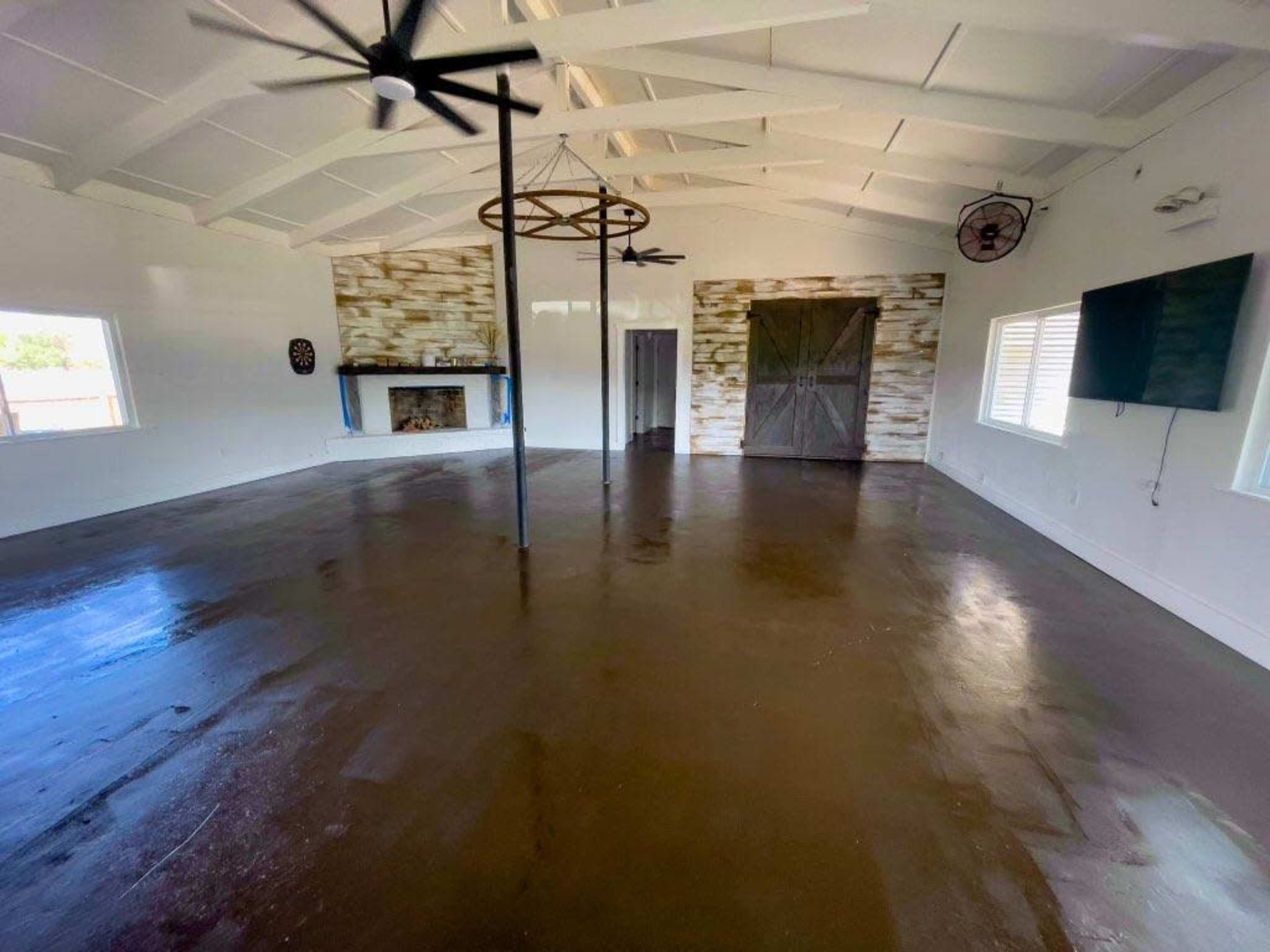 An open interior space with polished concrete flooring, a fireplace against a wooden accent wall, and ceiling fans overhead.