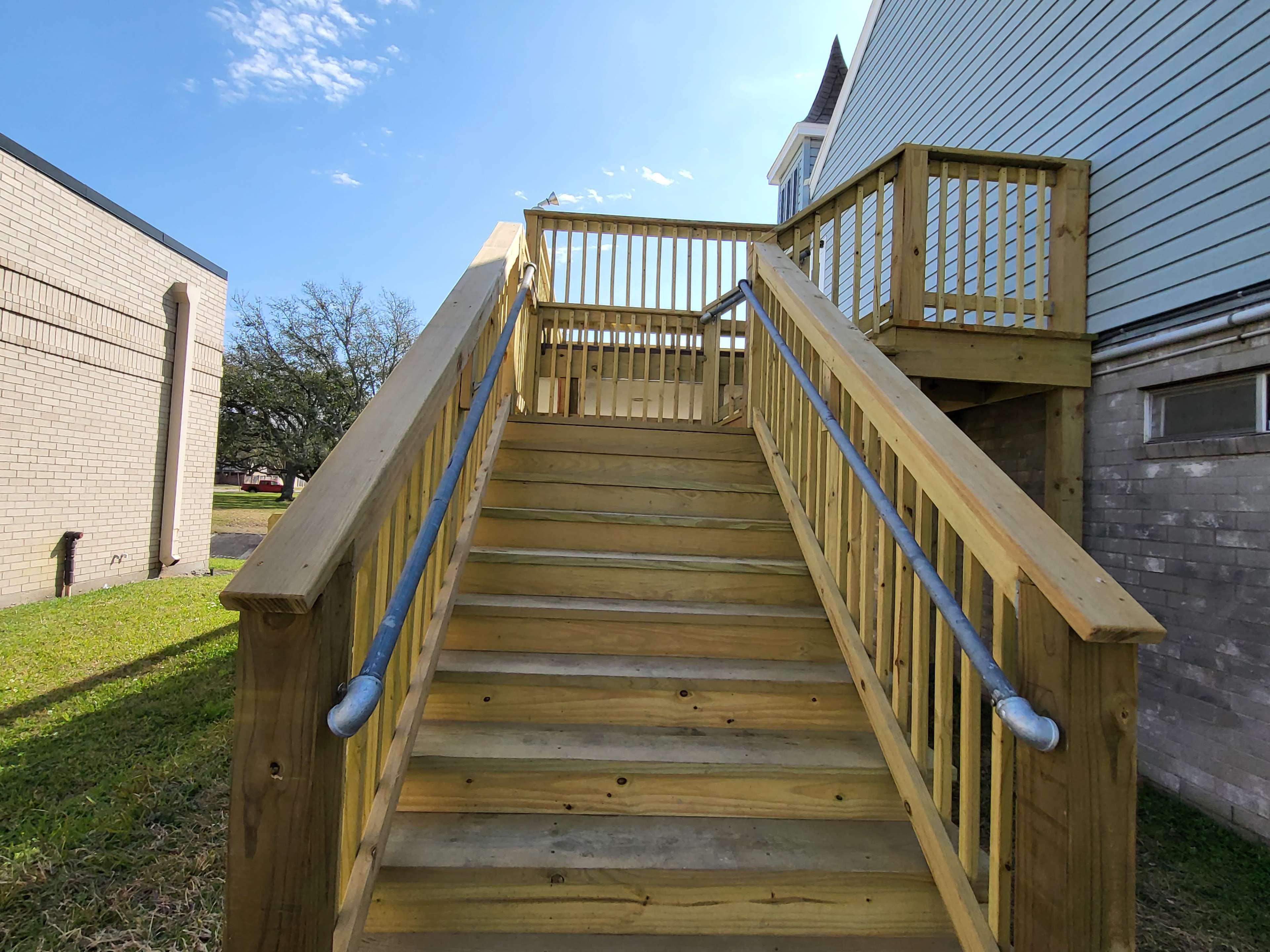 The image shows a wooden staircase leading up to a platform beside a light-colored building.
