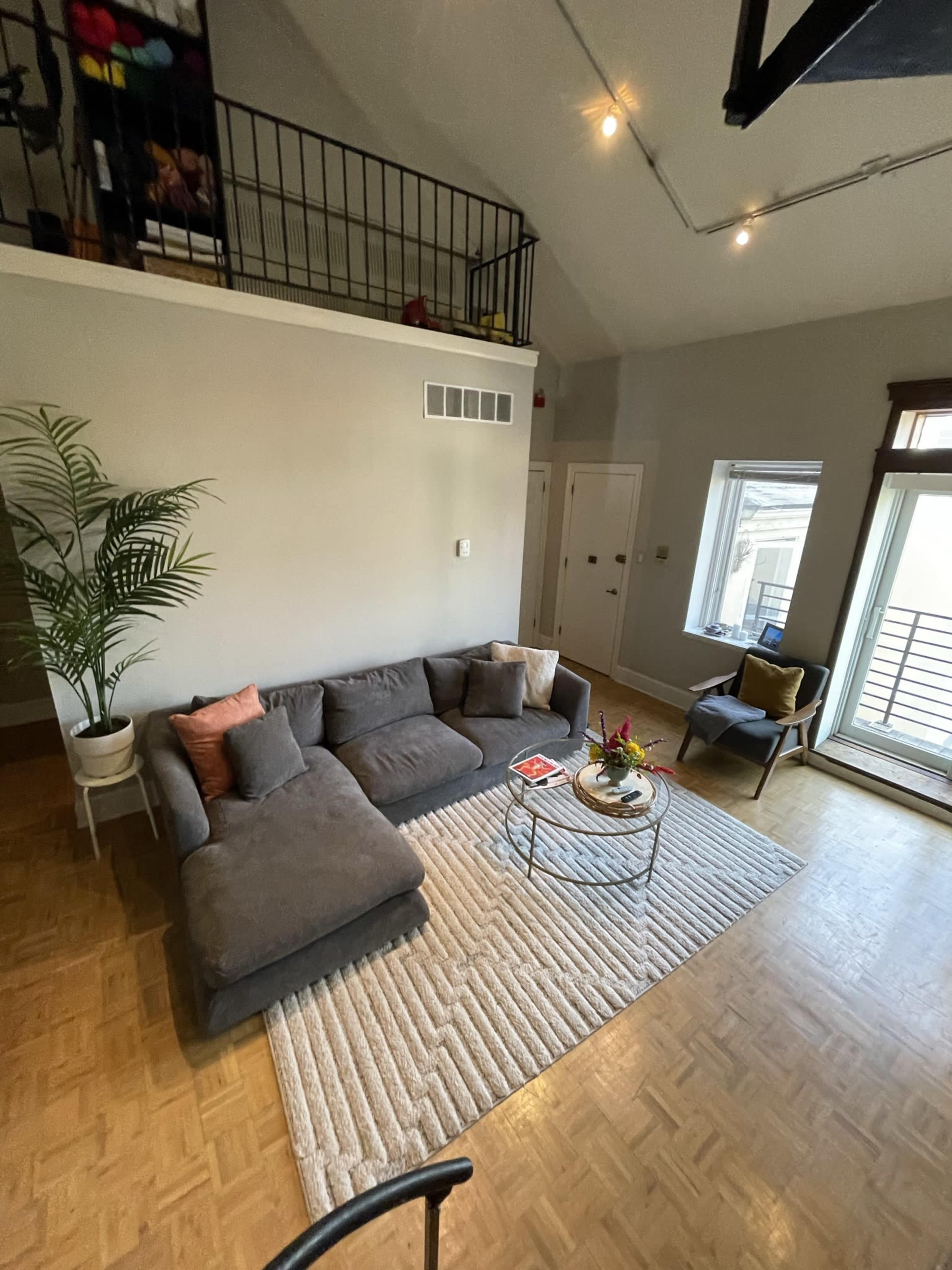 A modern living space features a gray sectional sofa, a round coffee table, and large windows with natural light.