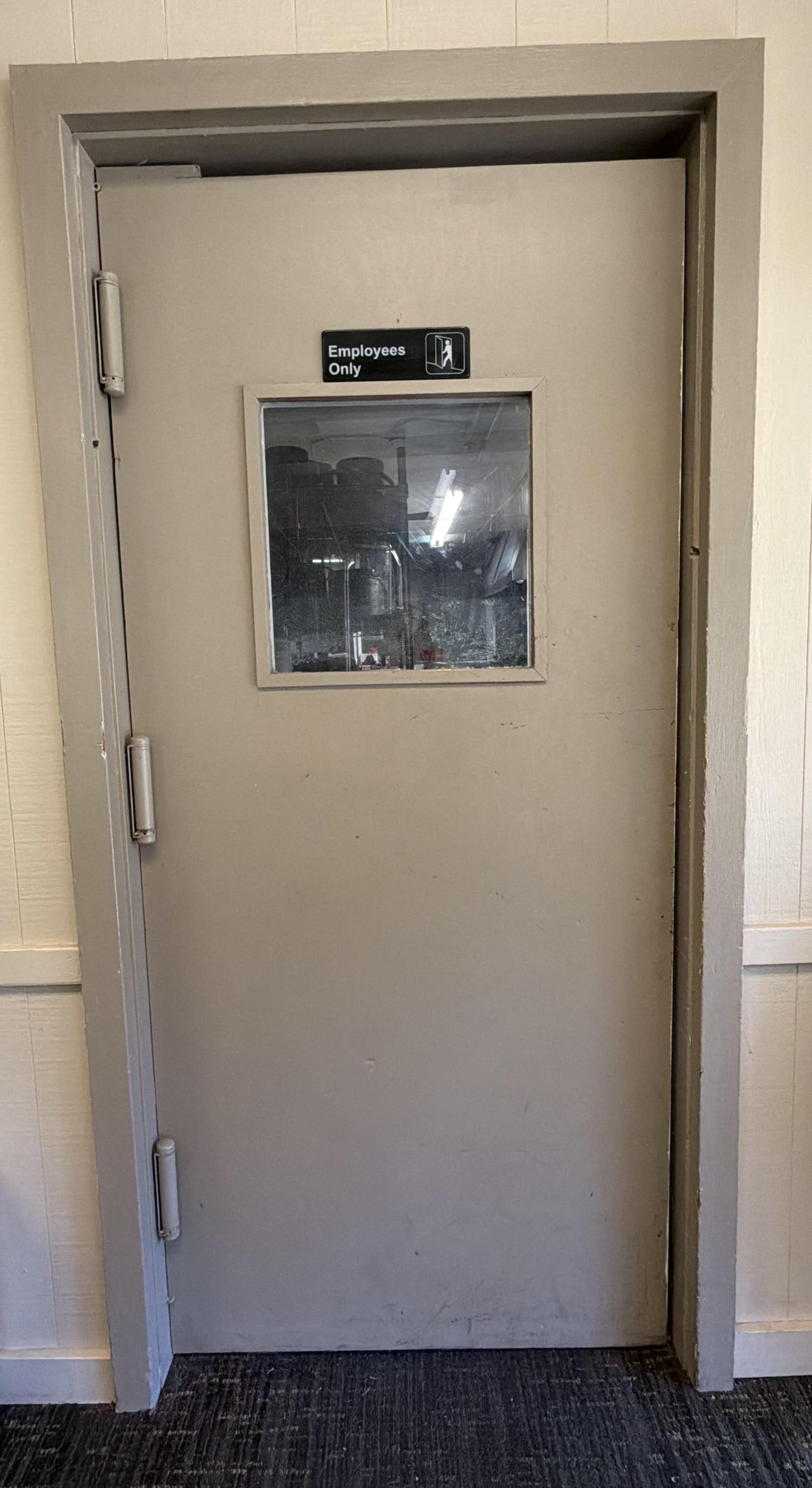 The image shows a gray door with a small window and a sign that reads "Employees Only."