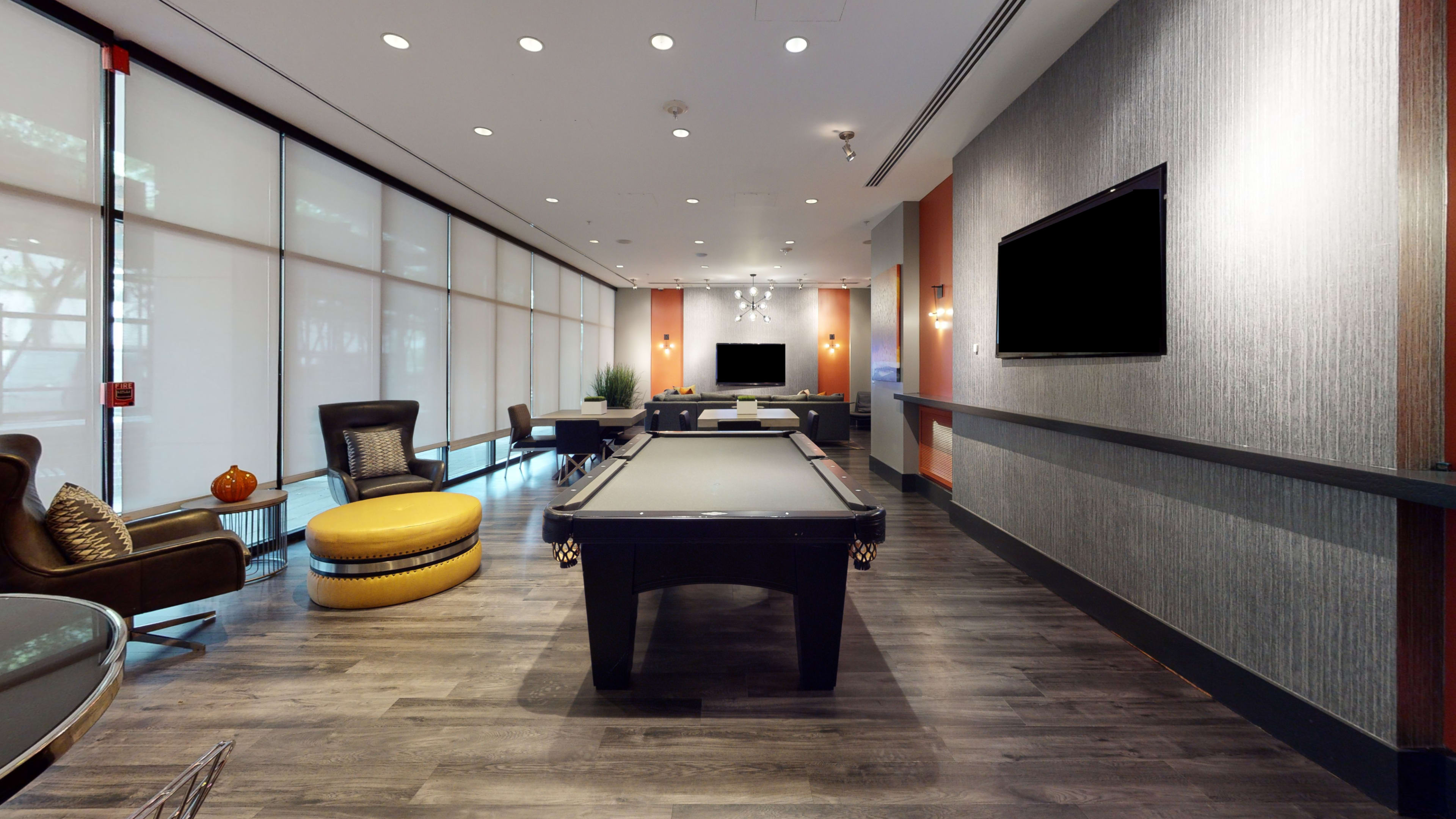 A well-lit lounge area featuring a billiard table, seating arrangements, and a large television mounted on the wall.