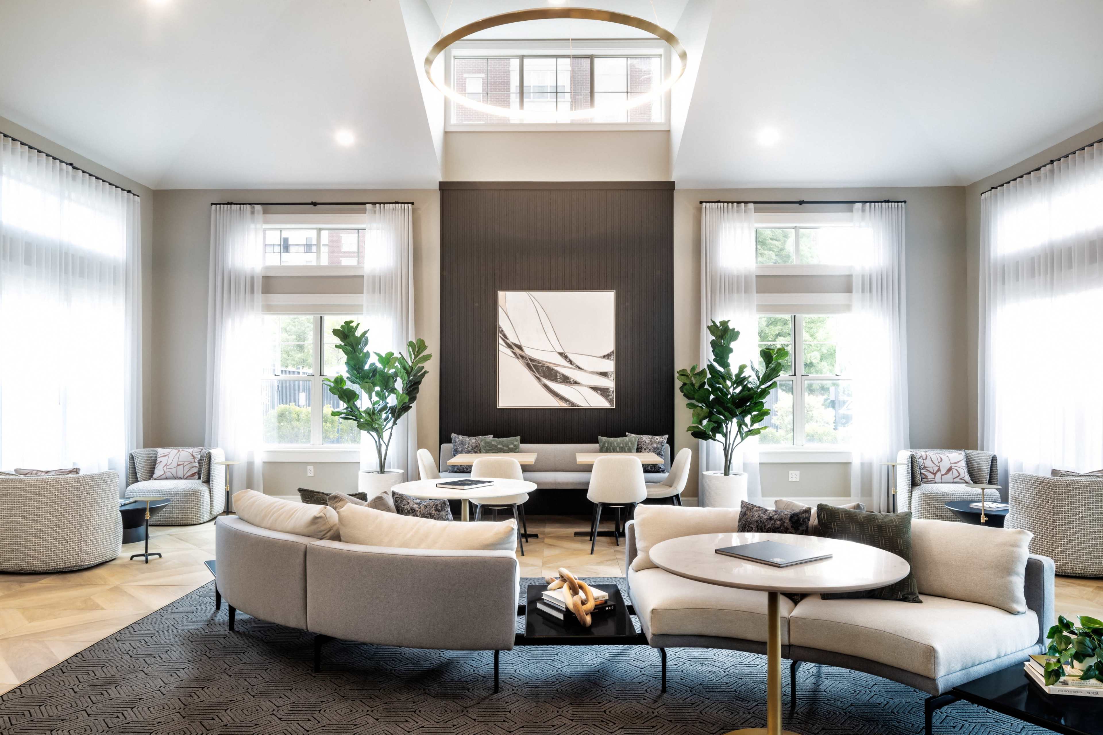 The image features a modern lounge area with large windows, stylish seating arrangements, and decorative plants.