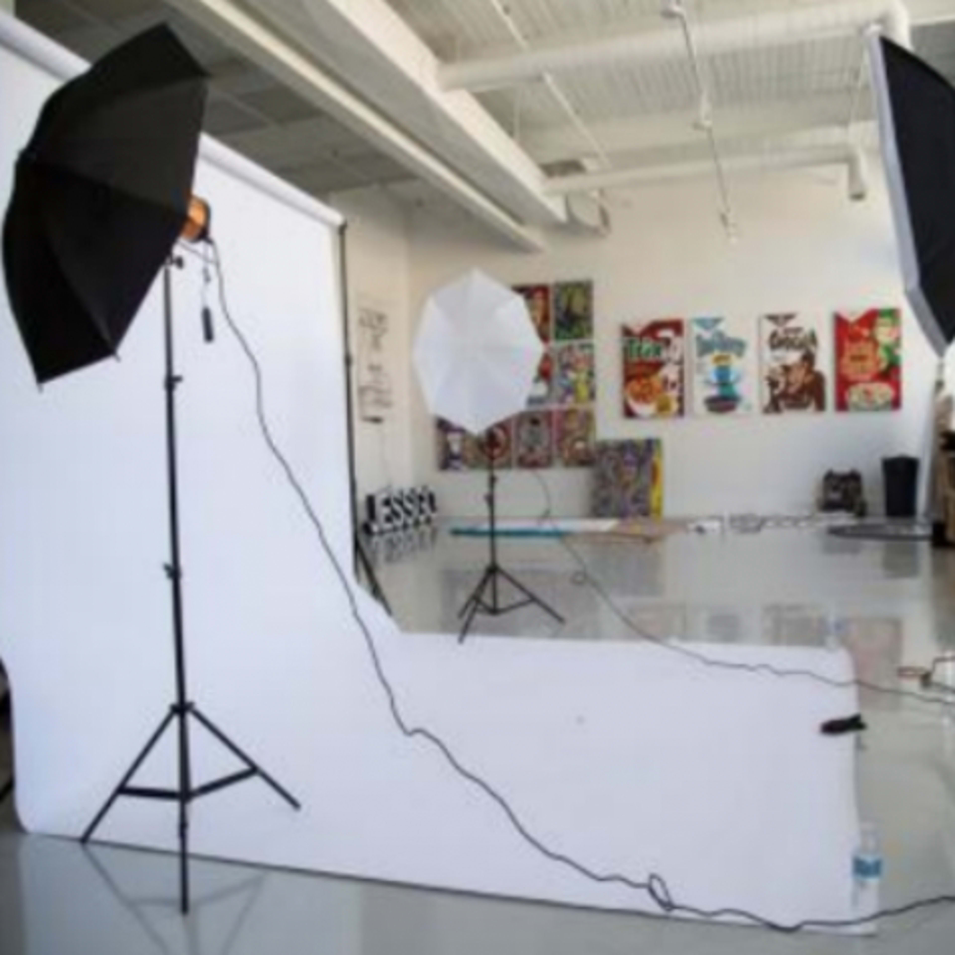 A photography studio setup with three light sources, two umbrella lights, and a white backdrop on a shiny floor.