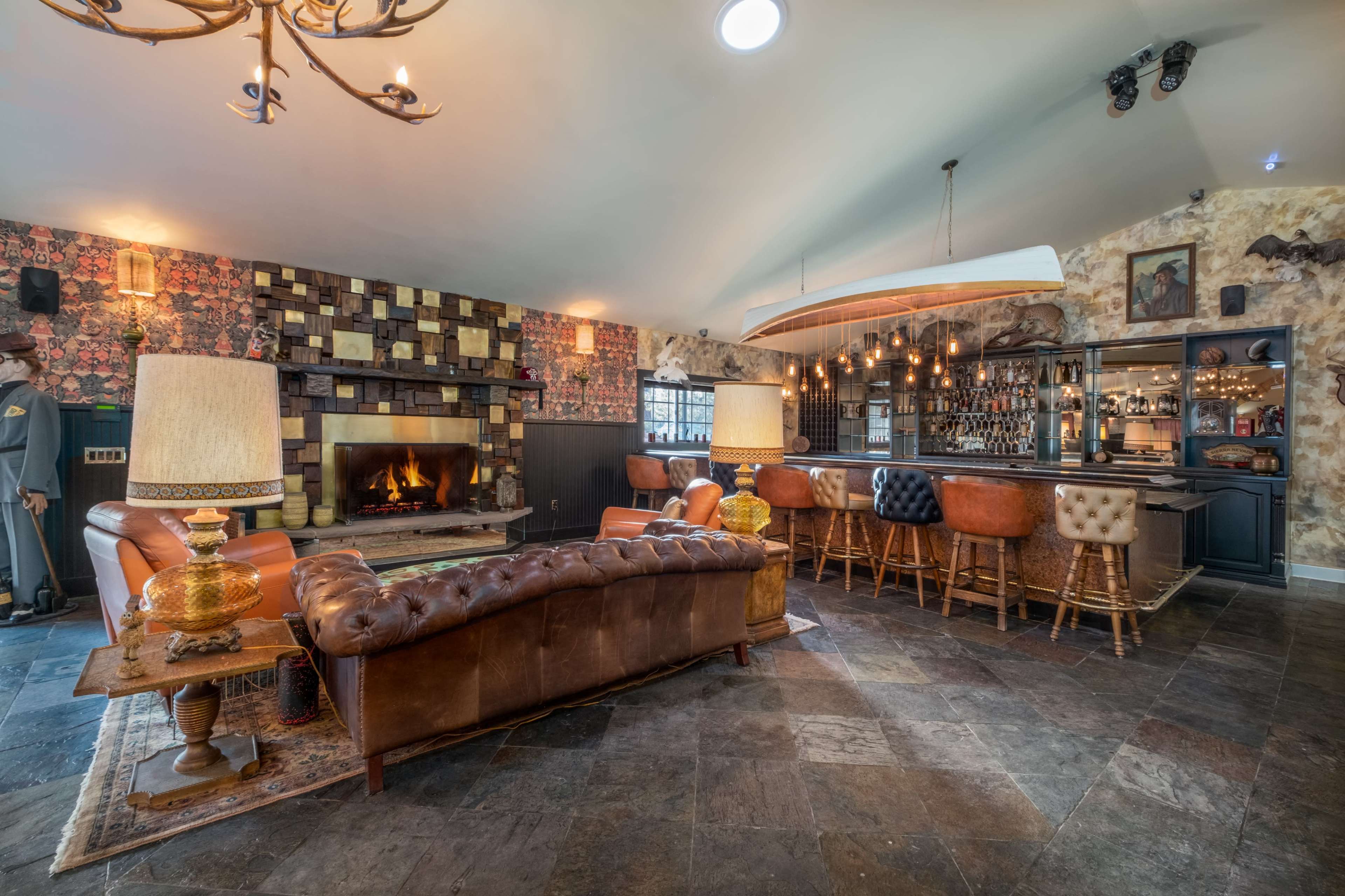A well-decorated lounge area featuring a leather sofa, a bar with various bottles, and a cozy fireplace against a patterned wall.