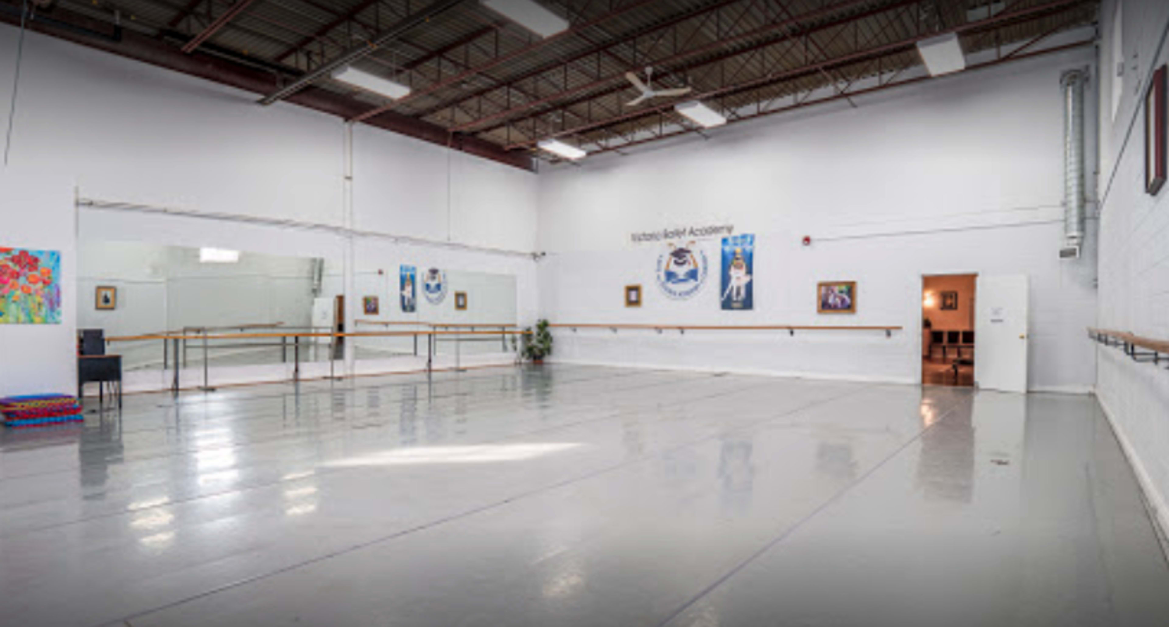 A spacious ballet studio with mirrored walls, ballet barres, and artwork displayed on the white walls.