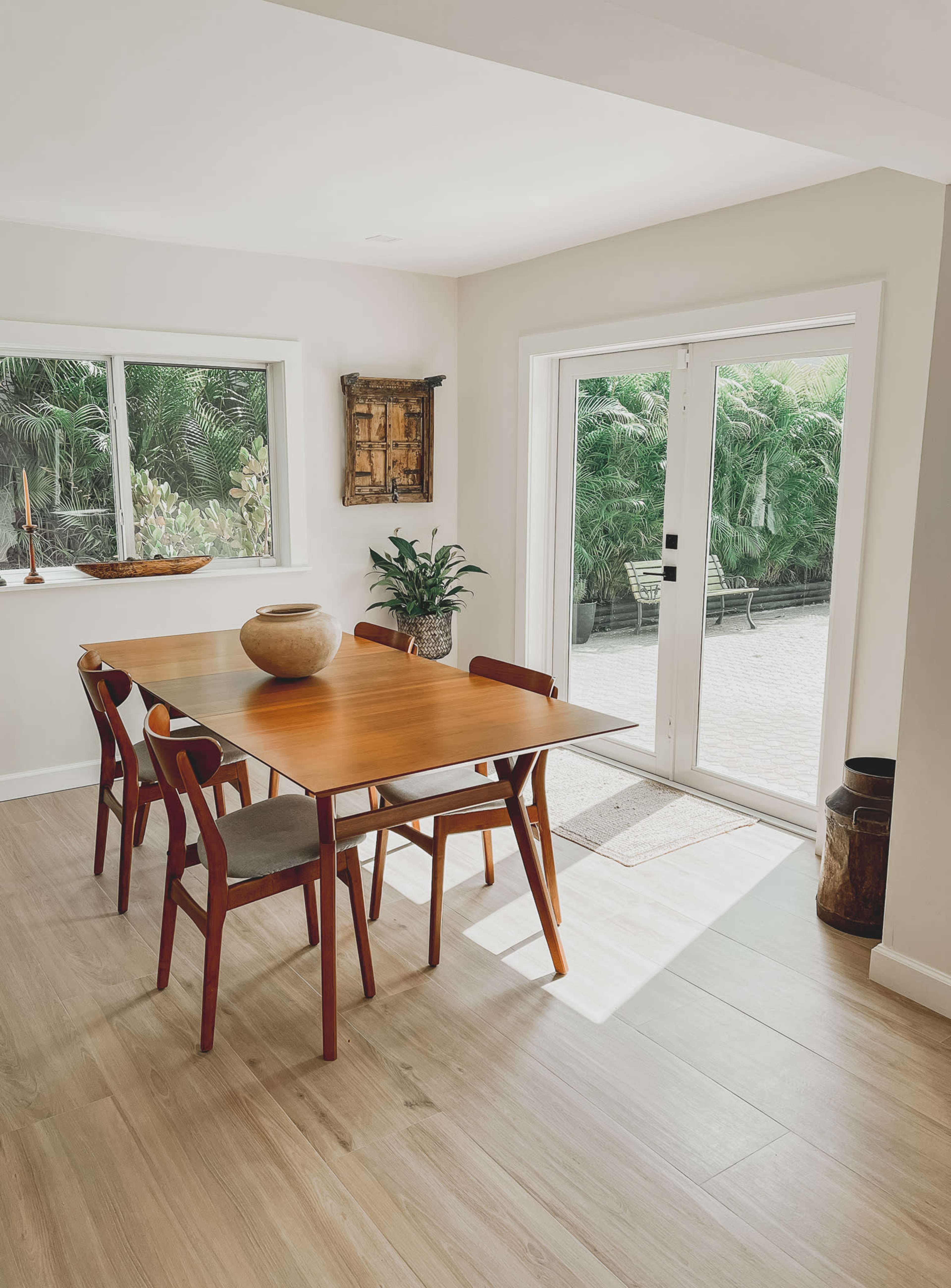 A dining area features a wooden table surrounded by four chairs and a large window overlooking a lush garden.