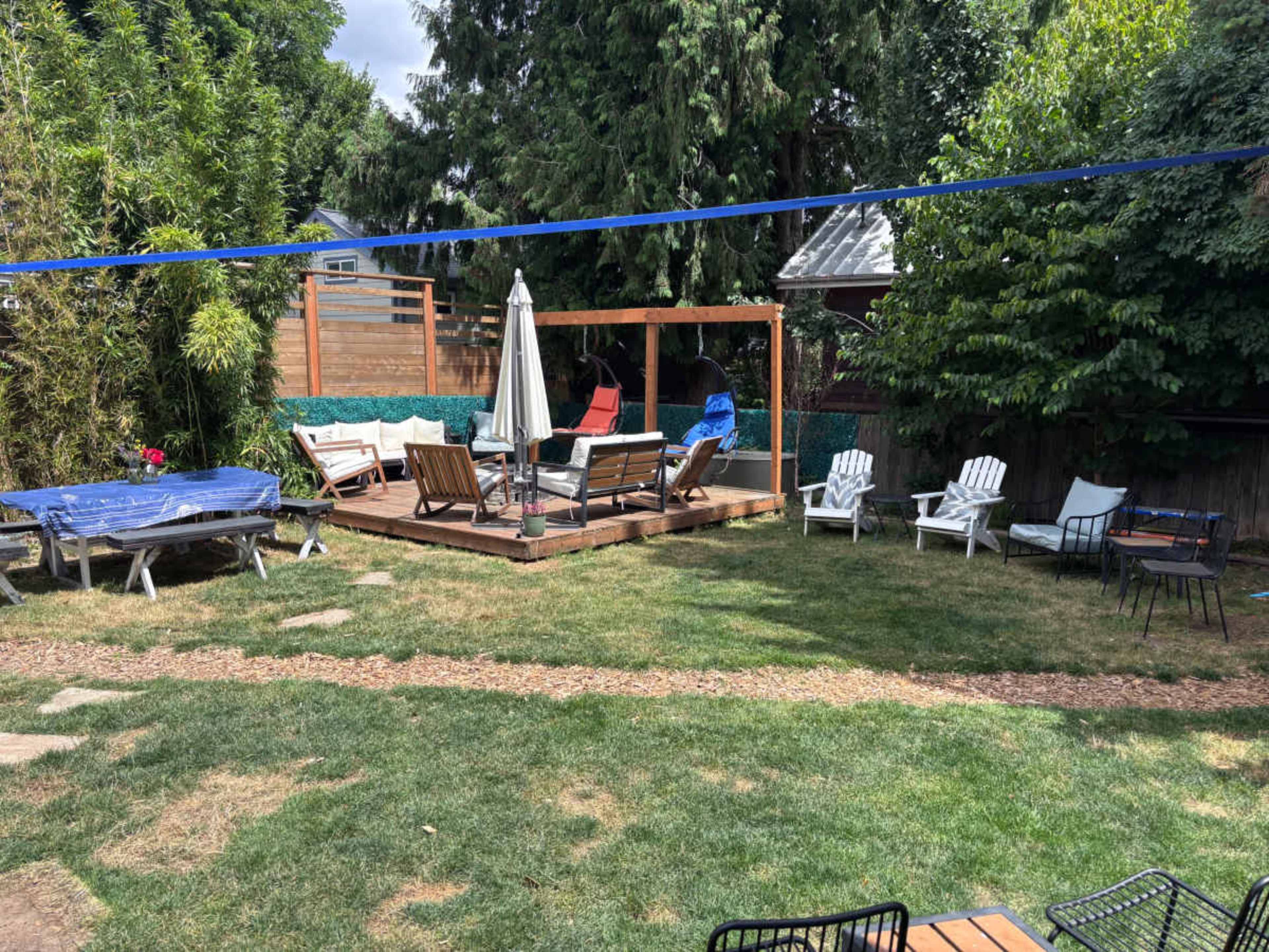 The image shows a backyard area with a wooden deck, various seating arrangements including lounge chairs and a table, and a laundry line running overhead.