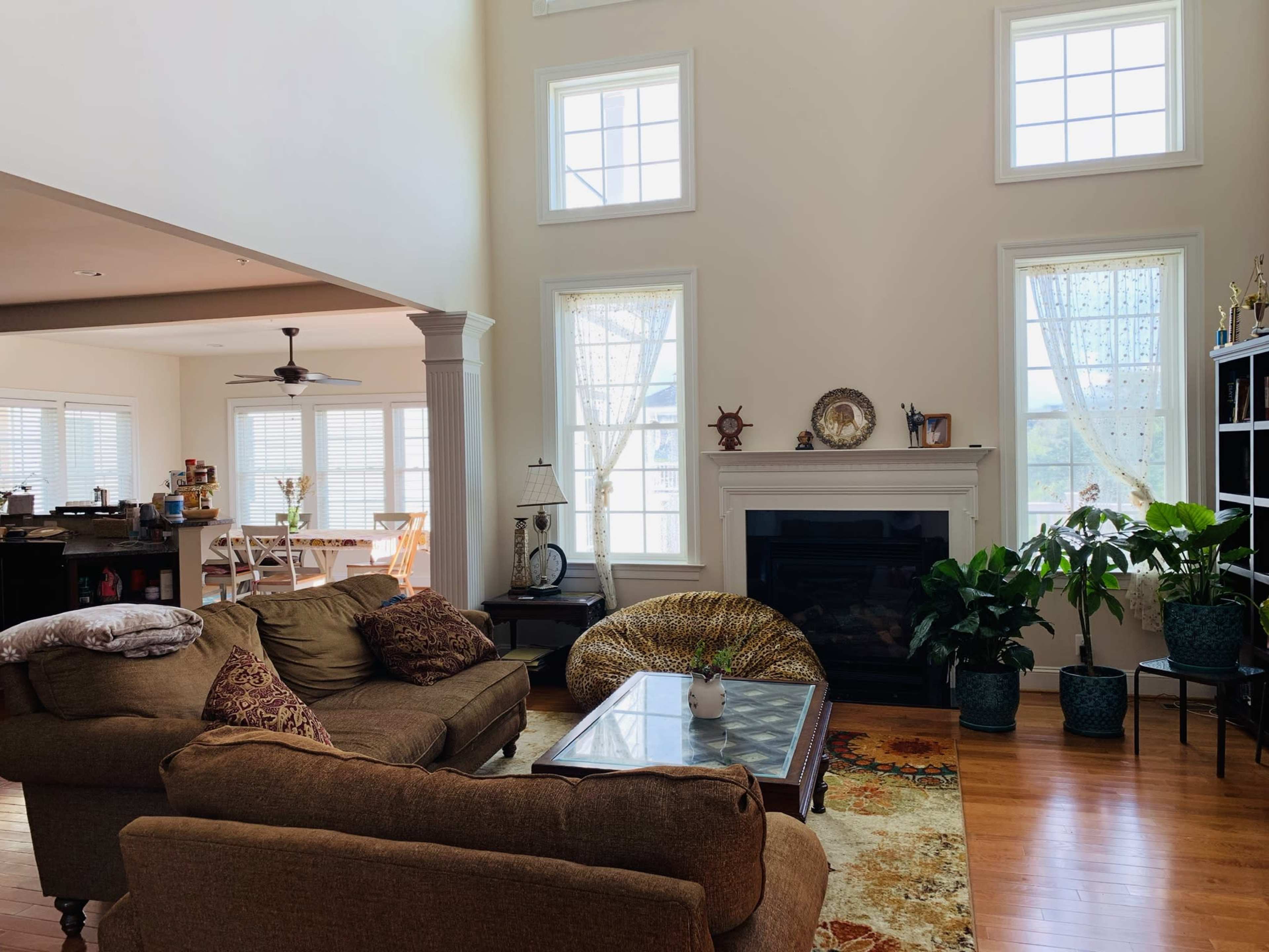 A spacious living room features a large sofa, a glass coffee table, and windows that allow natural light to fill the space.